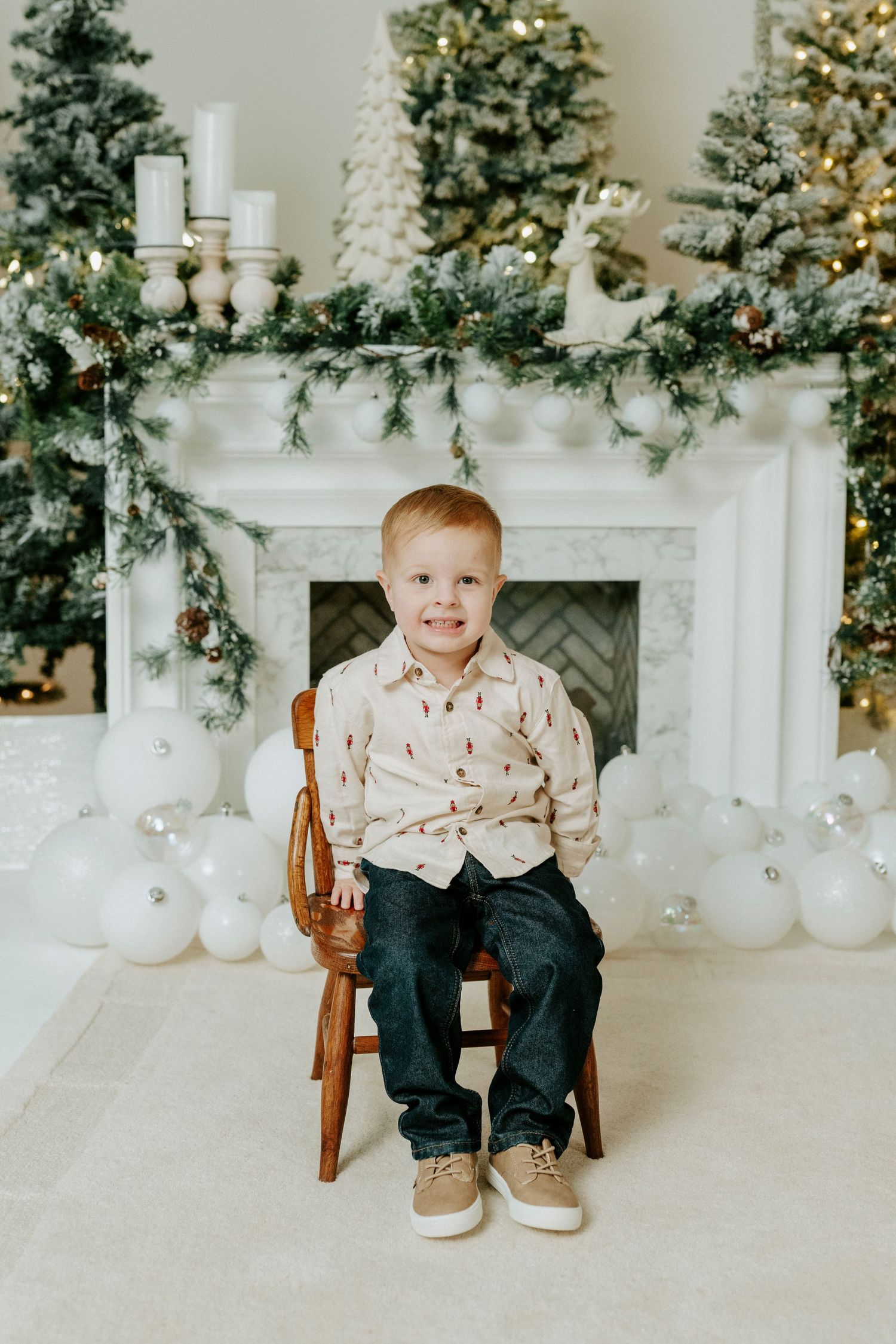 A festive holiday scene with decorated Christmas trees and a white fireplace mantel adorned with garland and white balloons.