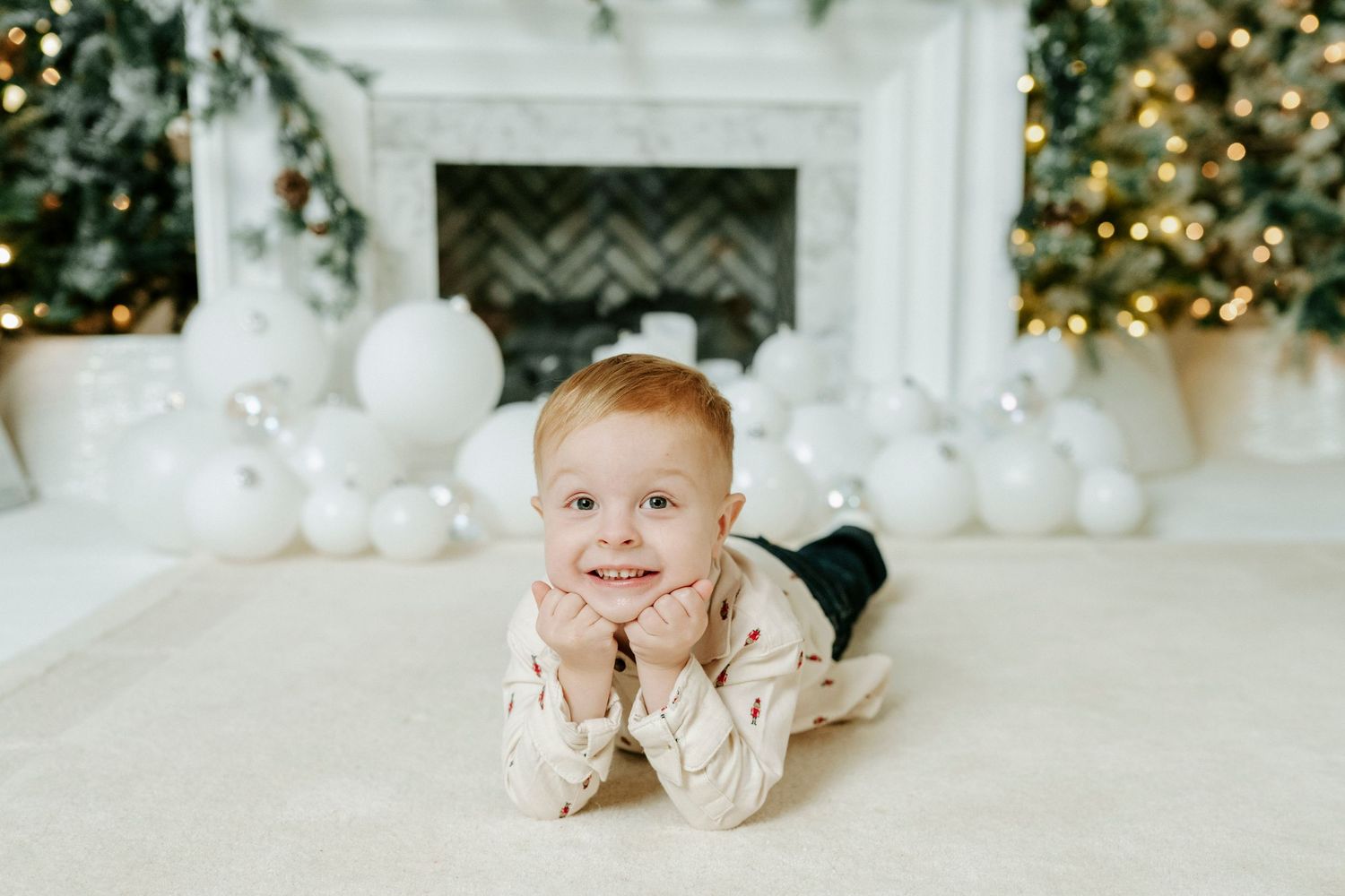 A white and gold themed holiday photoshoot setup with Christmas trees, ornaments, and festive decorations.