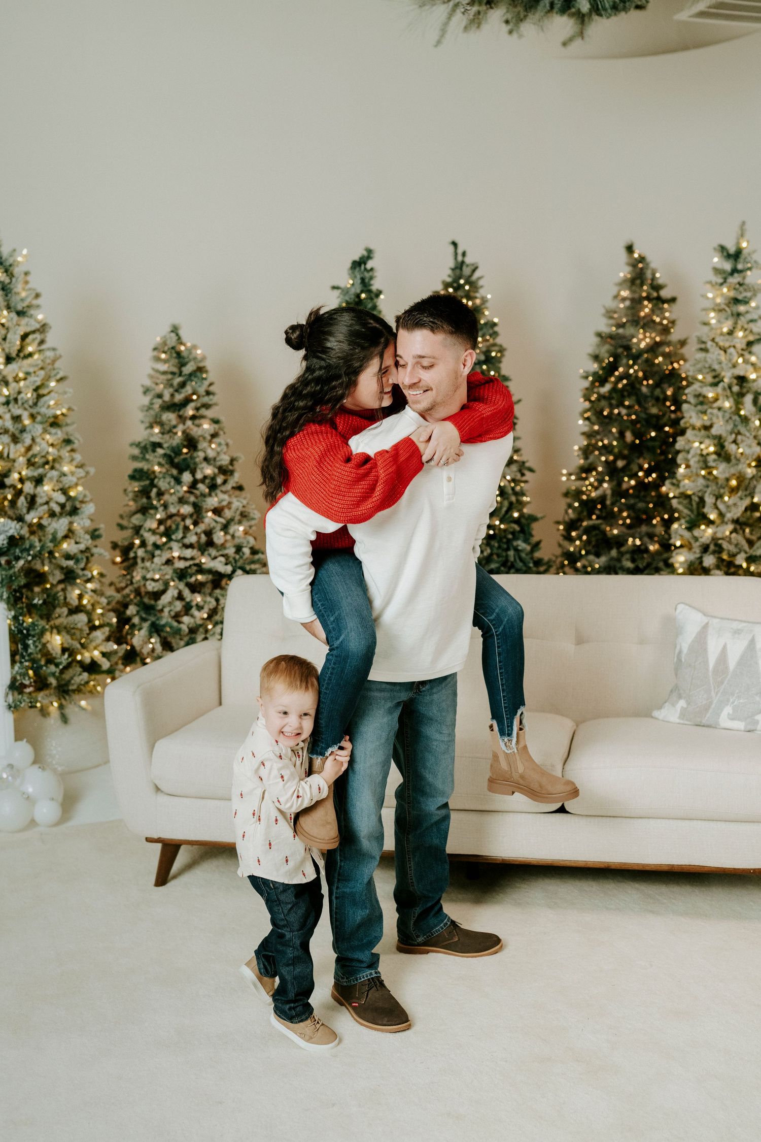 A parent and child share a tender moment on a white couch with decorated Christmas trees in the background.