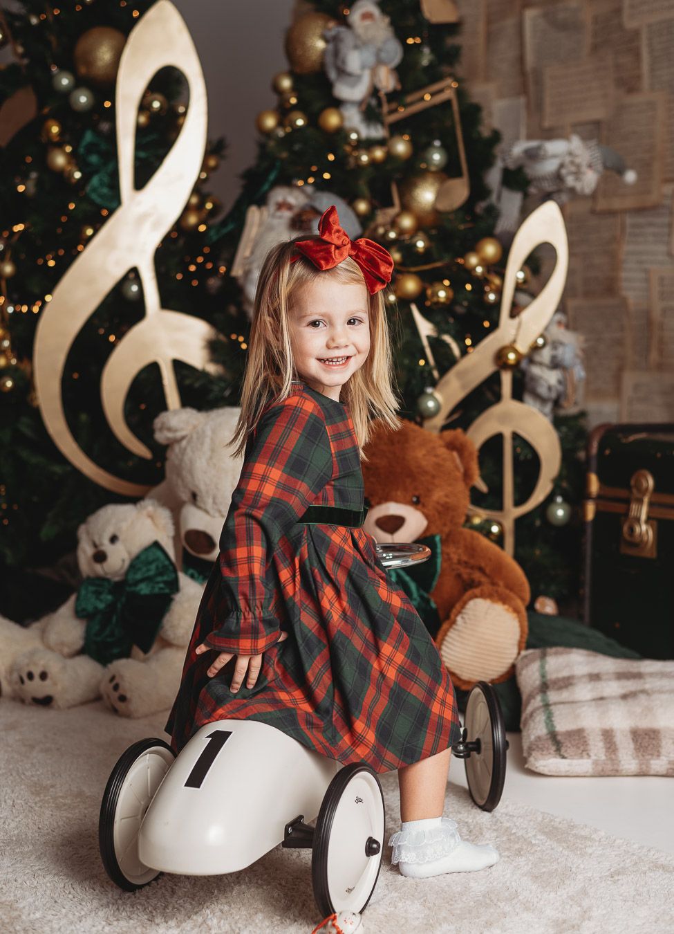 A series of four photos showing a child in plaid dress playing with a rocking horse against a Christmas tree backdrop.