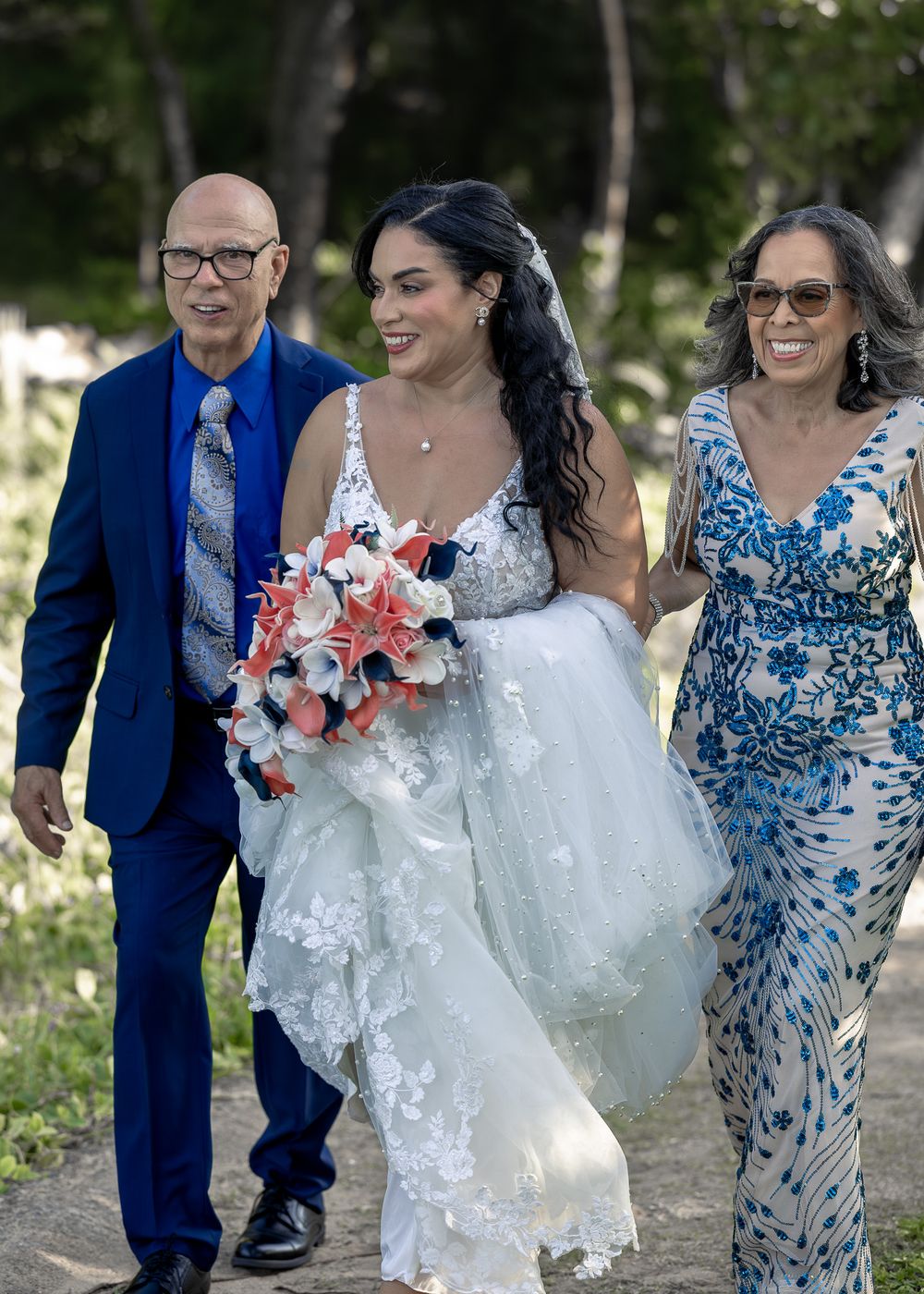 Wedding party members walk together outdoors wearing blue attire and white dresses in a natural setting.