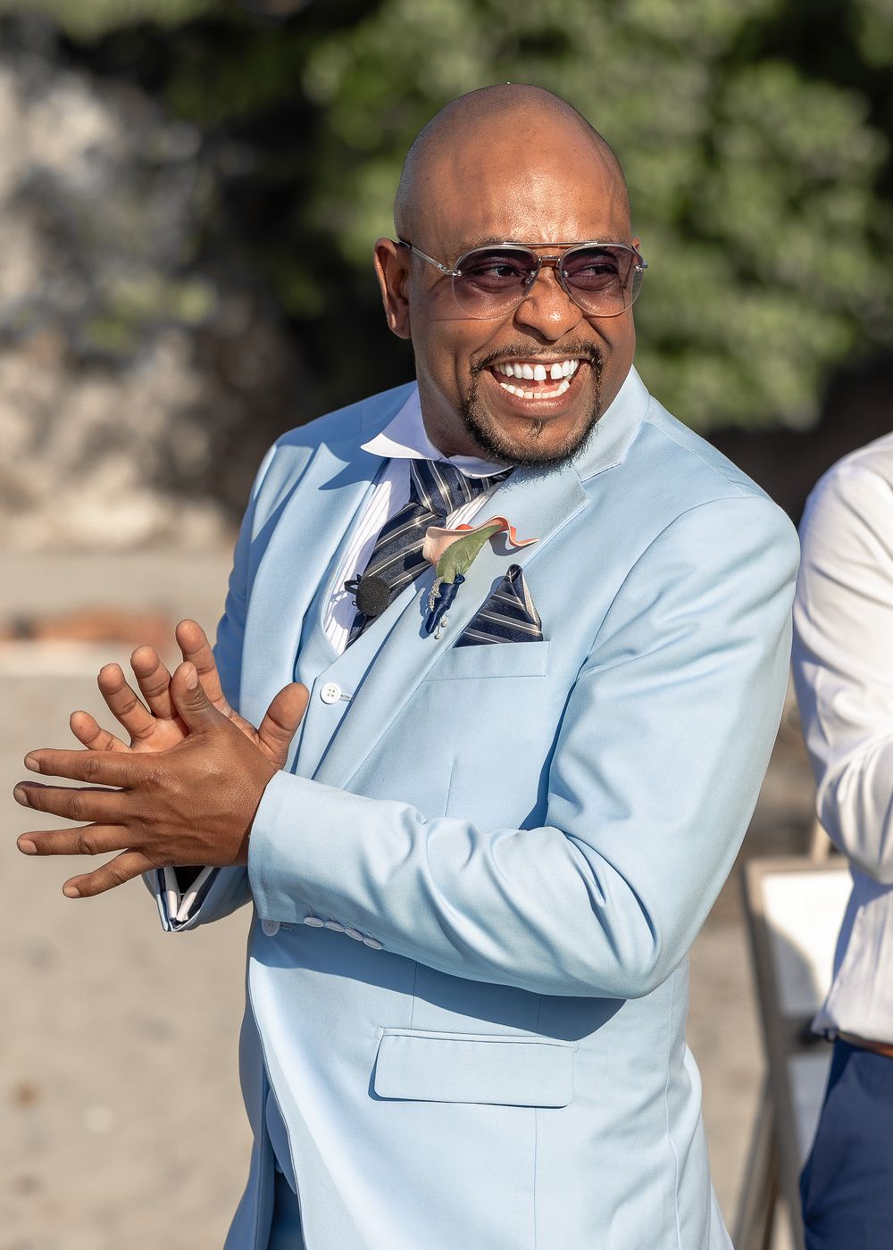 Person in light blue suit jacket making expressive hand gestures while speaking outdoors.
