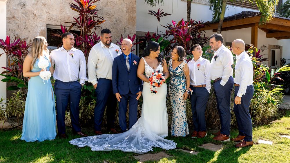 Wedding party members in blue and gray attire pose together in a lush tropical garden setting.