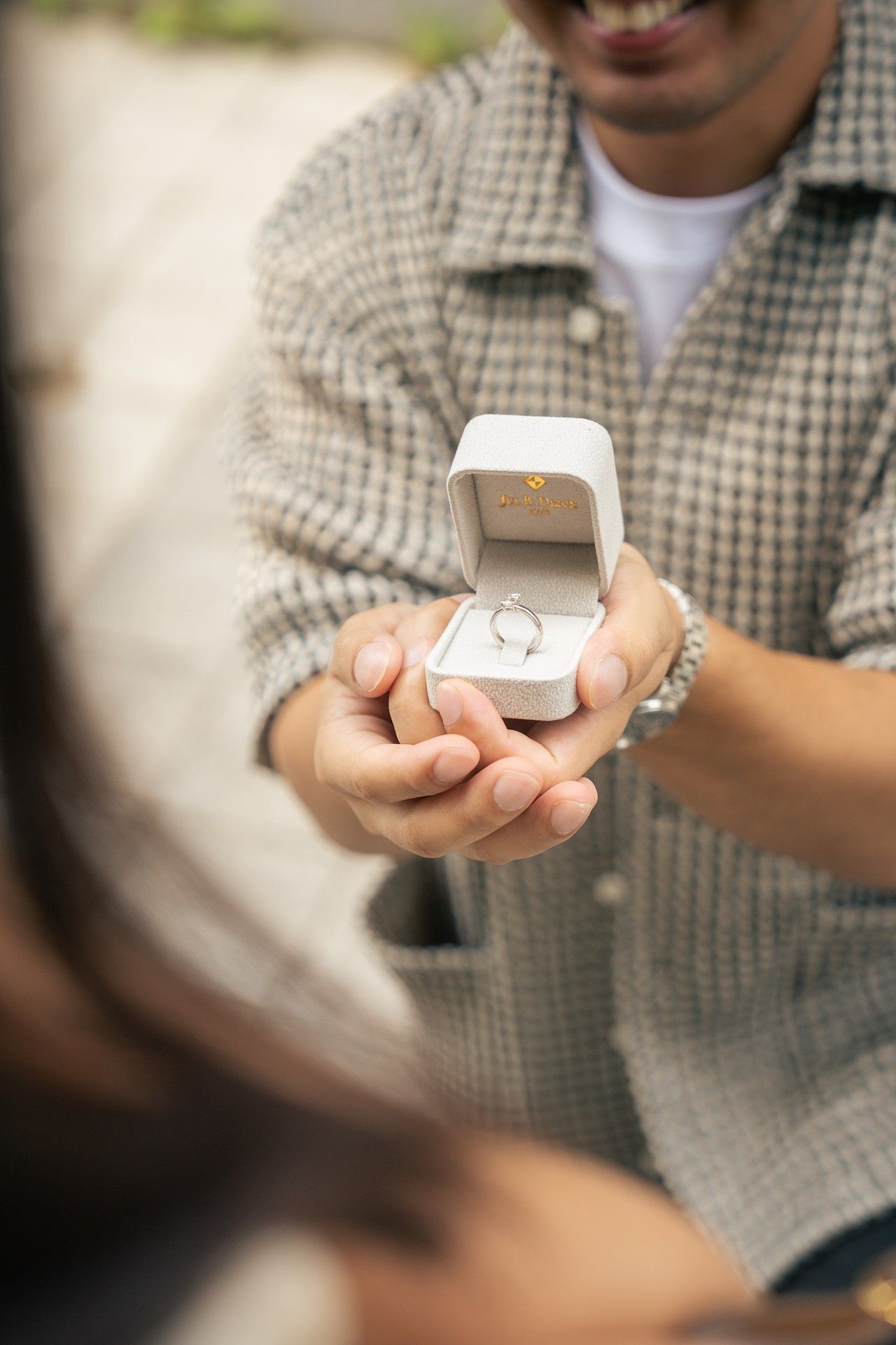 A person in a checkered shirt holds a small white box with a ring inside, photographed in a sequence of images.
