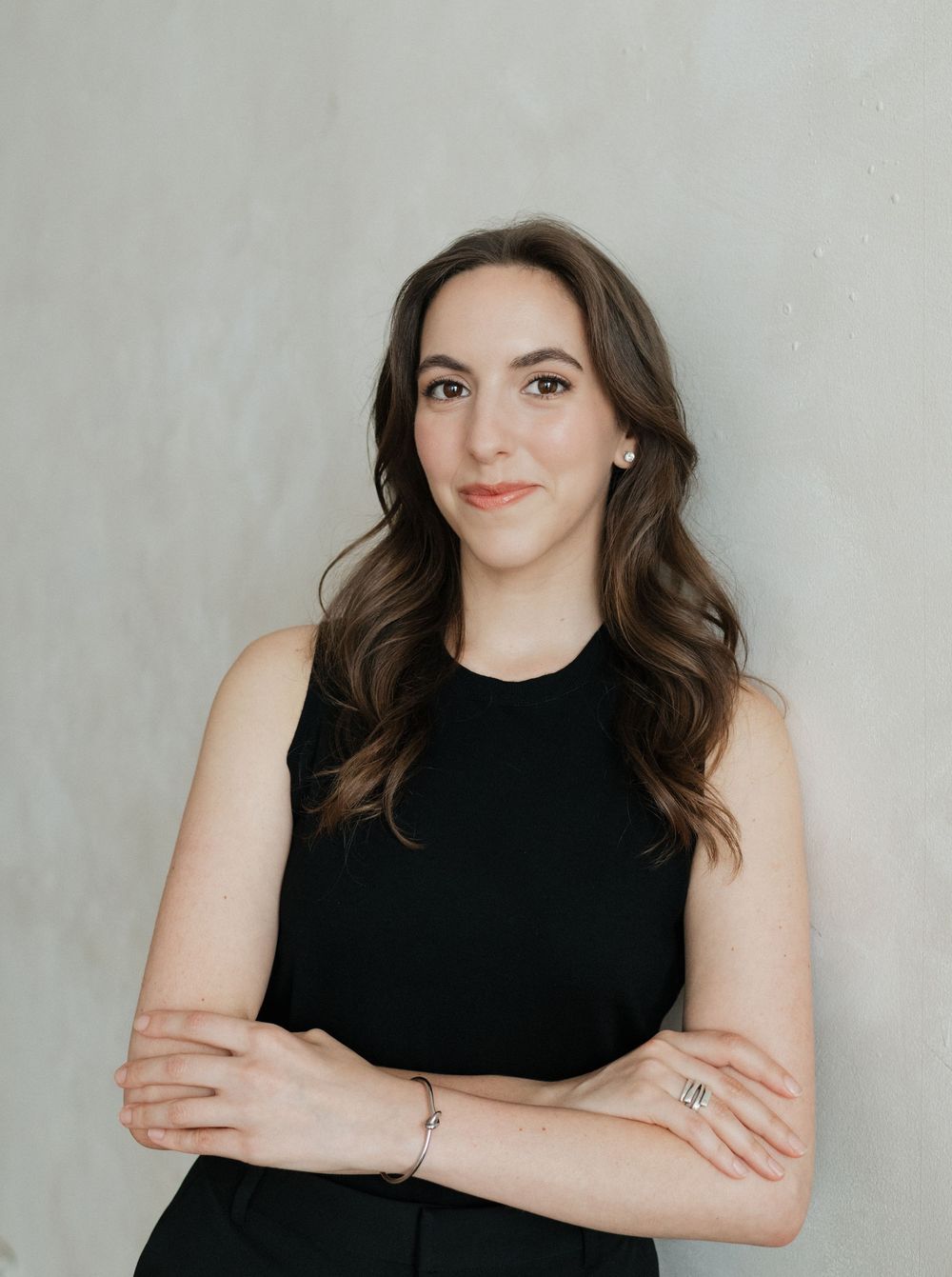 Professional woman in black sleeveless top with crossed arms, smiling confidently against a neutral gray background.