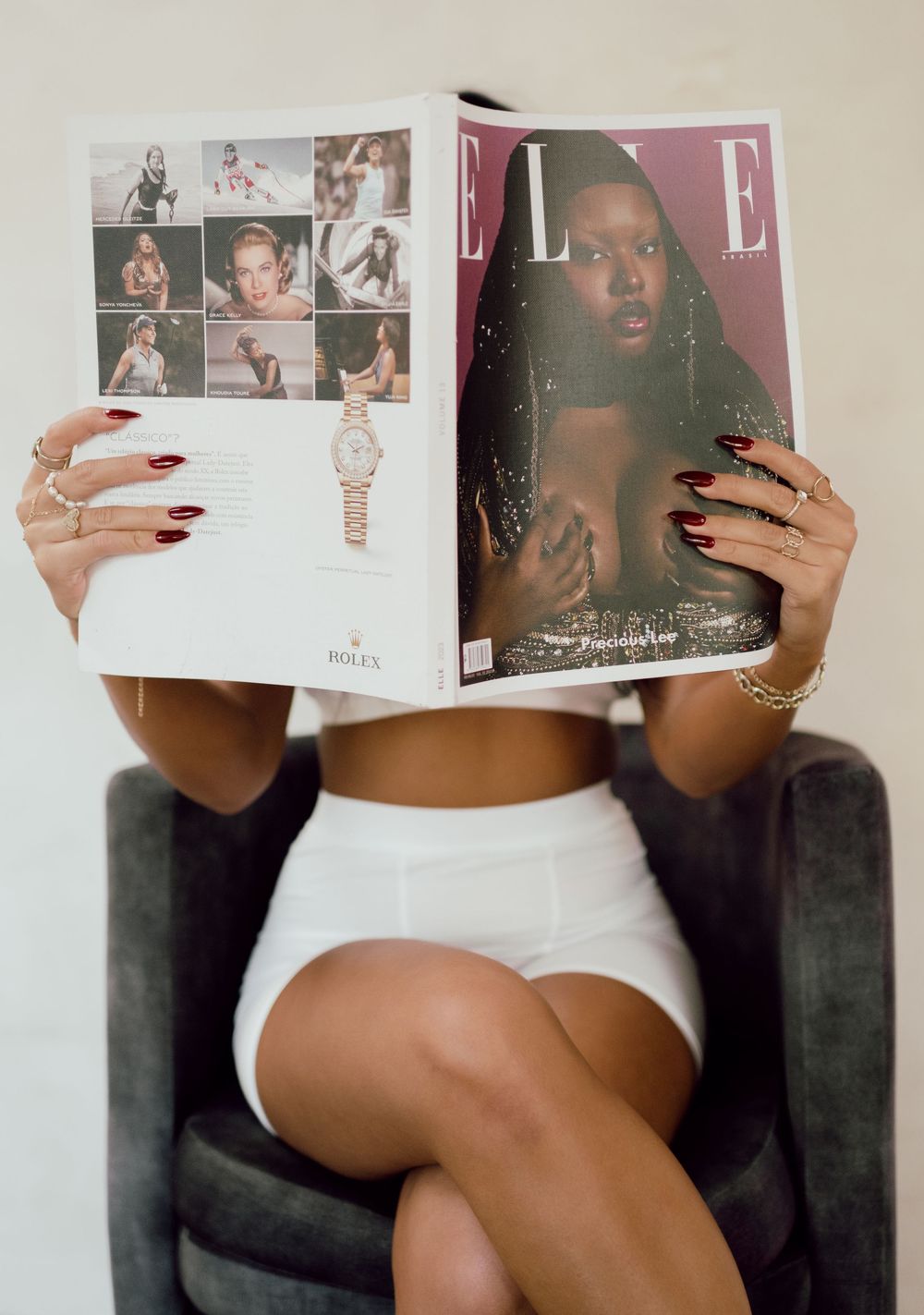 Person holding fashion magazines while sitting on dark couch.