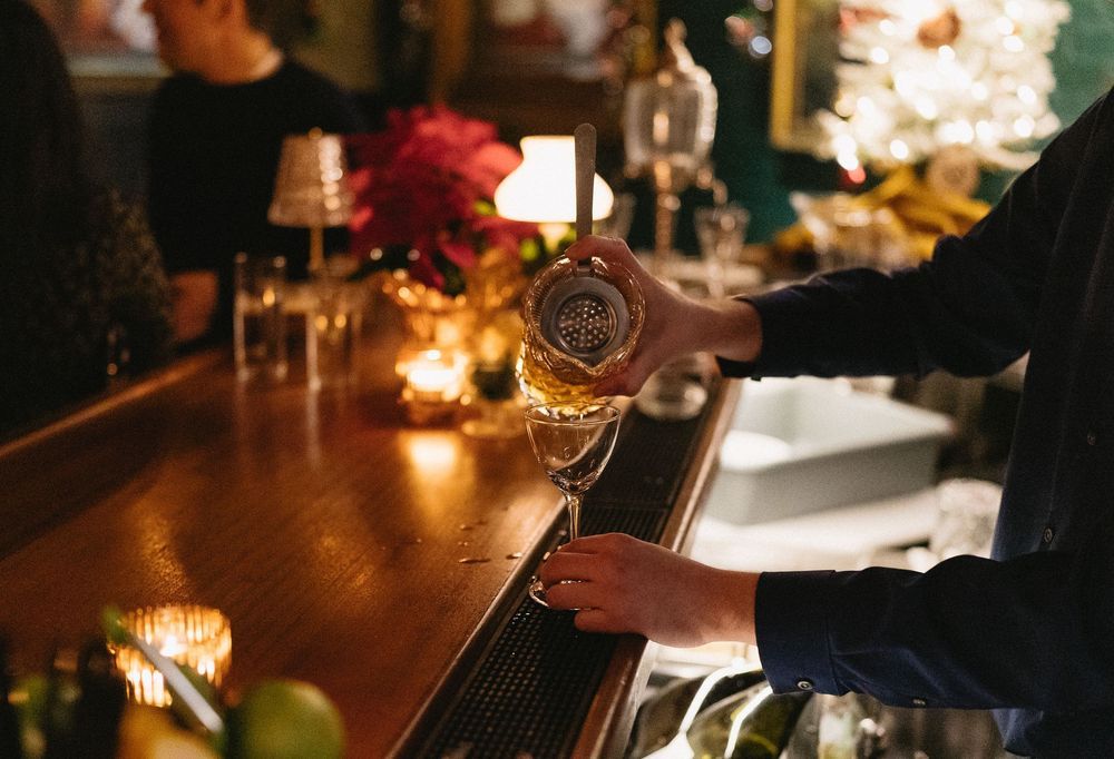 Bartender pouring white wine into a glass at a warmly lit bar with candles and floral decorations.