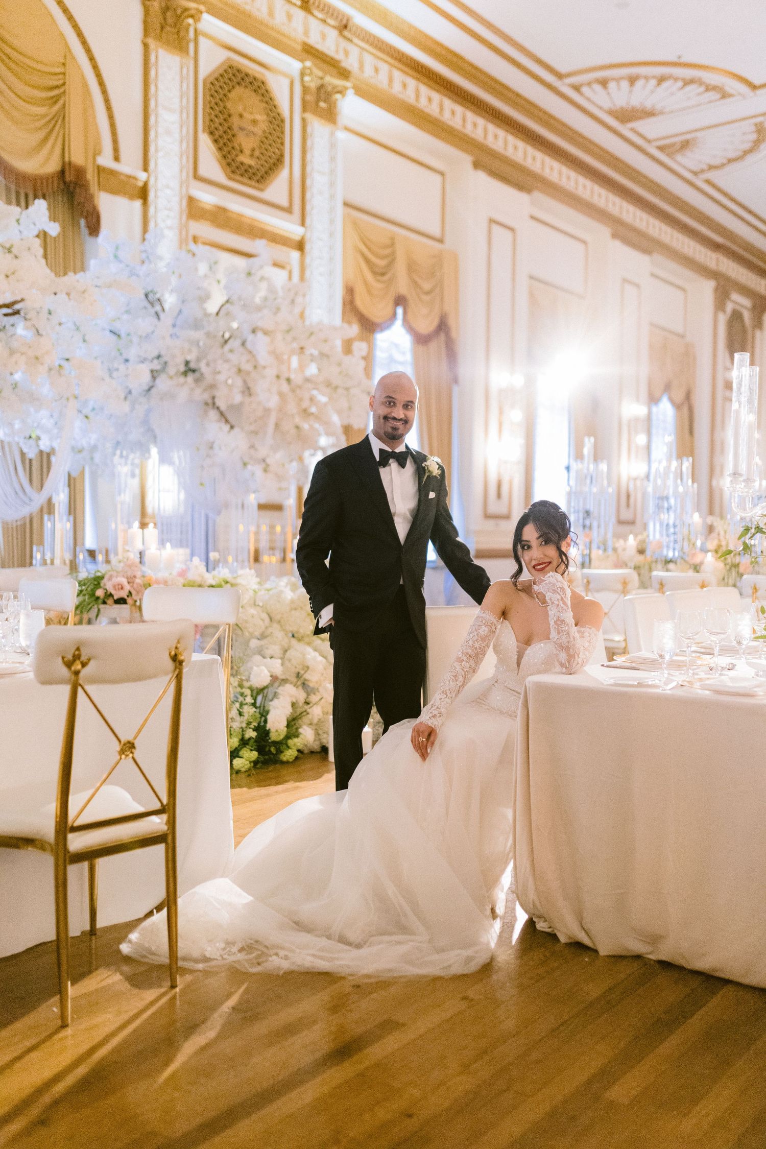 Elegant wedding reception setup in a grand ballroom with crystal chandeliers and white floral arrangements.