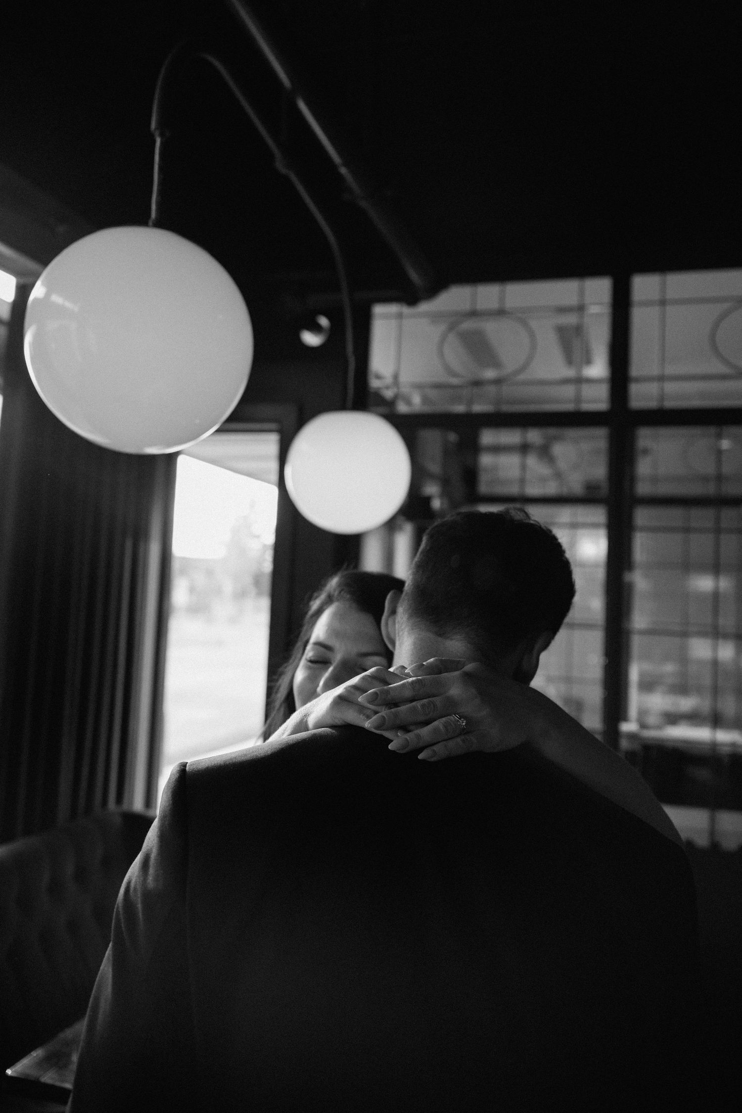 Black and white photo of a romantic moment under round pendant lights in a dimly lit interior space.