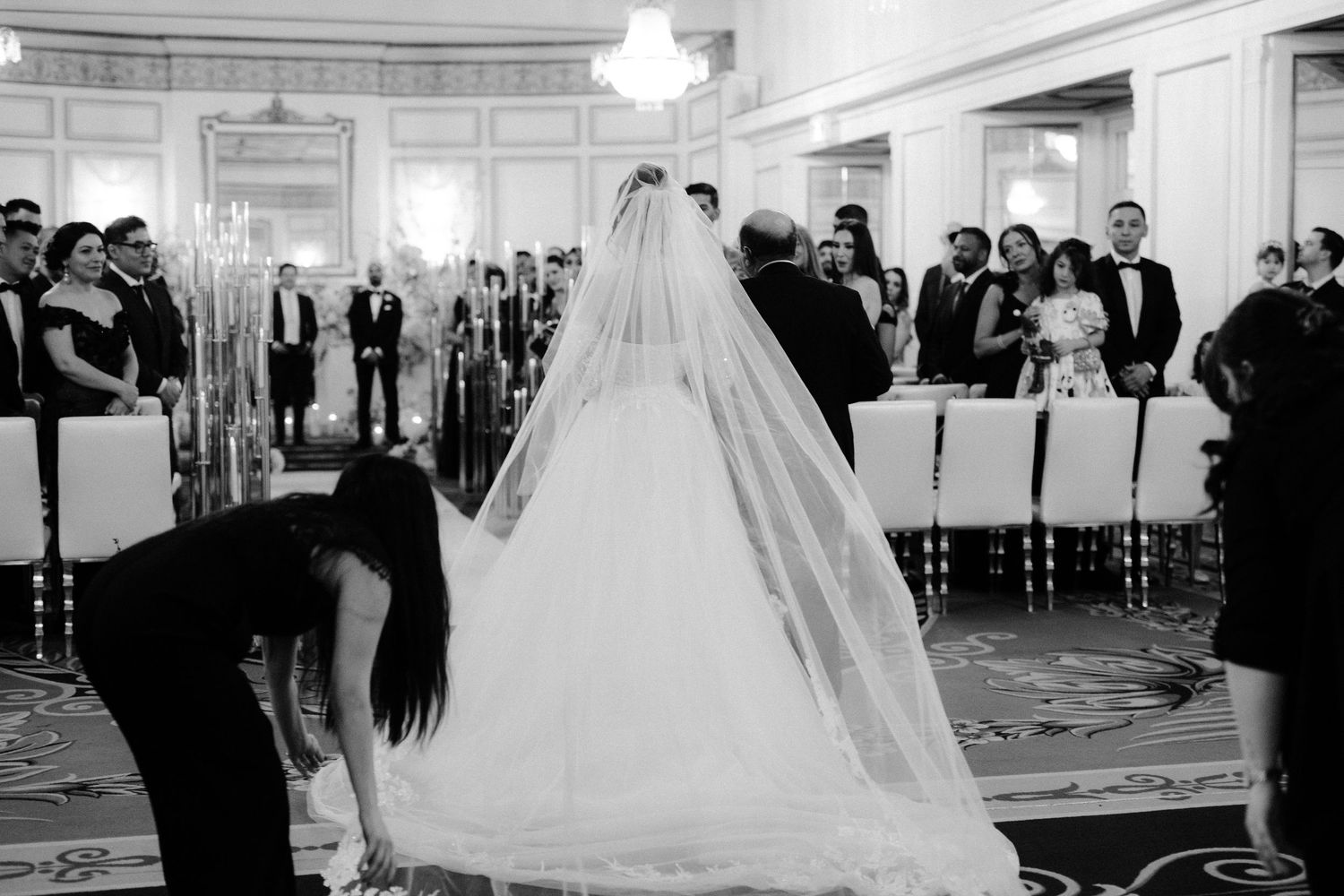 A wedding ceremony in a grand ballroom with guests watching as the bride and groom exchange vows under elegant lighting.
