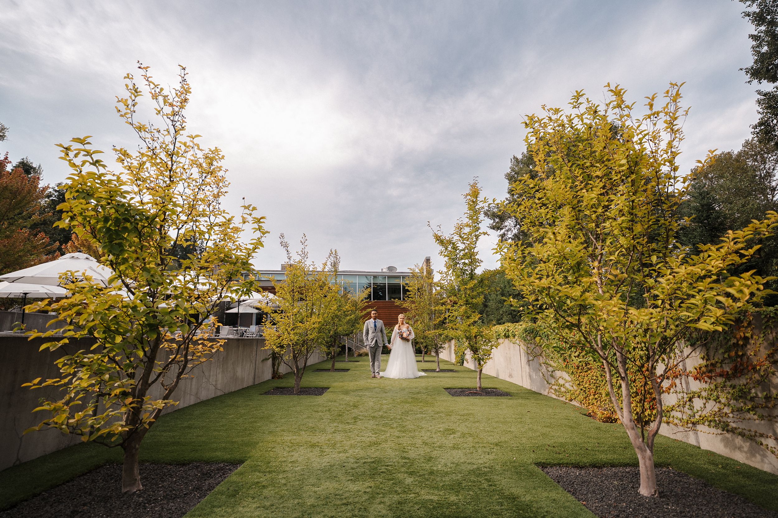 Autumn wedding ceremony setup with yellow trees lining a grassy aisle under cloudy skies at an outdoor venue.