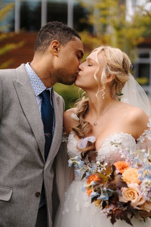 A romantic wedding couple shares a tender kiss while holding a beautiful peach and white floral bouquet.
