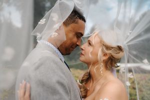 A romantic couple in wedding attire share an intimate moment under a flowing veil on their special day.