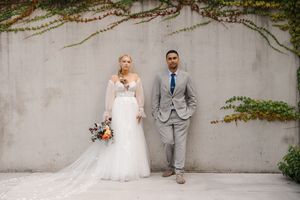 A bride and groom stand together against a concrete wall with climbing vines creating an elegant outdoor setting.