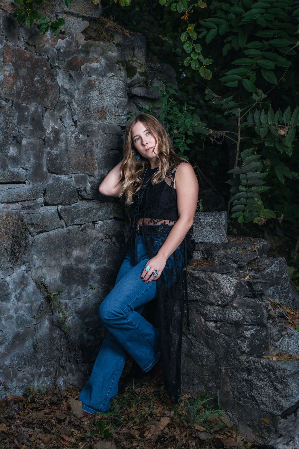 Casual fashion pose against rustic stone wall backdrop with lush green foliage.