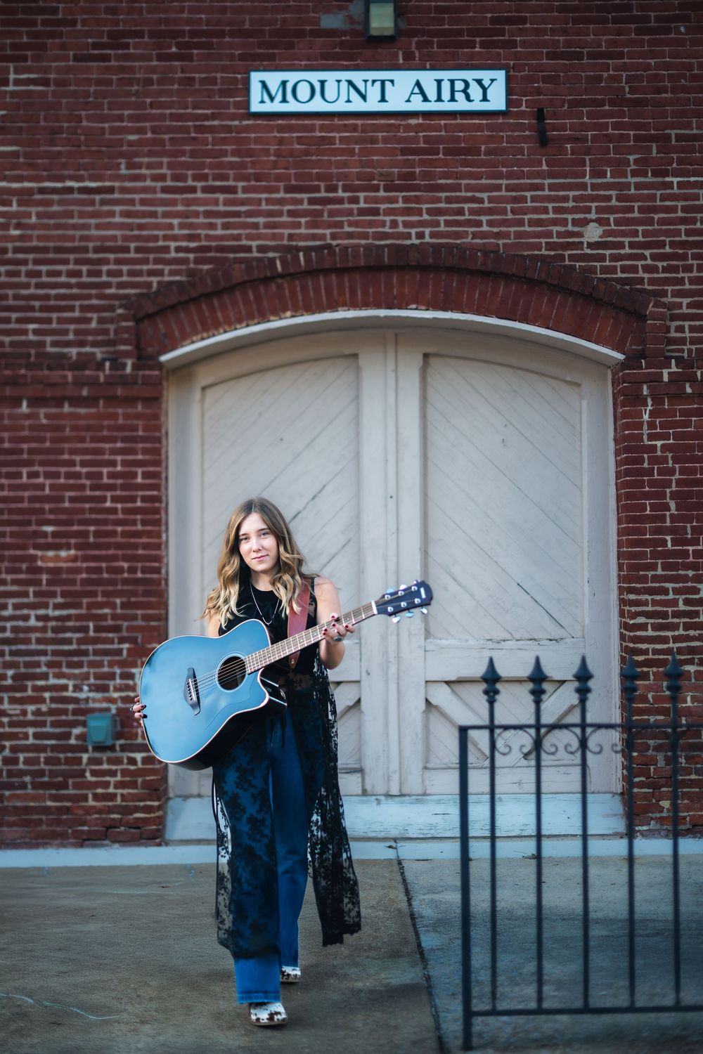A series of artistic portraits against a brick wall with Mount Airy signage featuring a musician with a blue guitar.