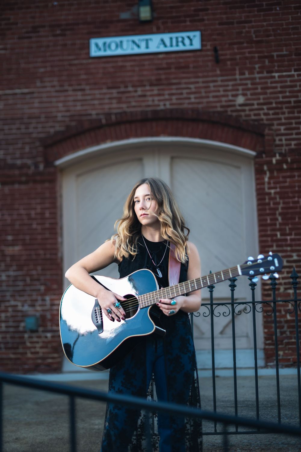 A musician plays an acoustic guitar against a brick wall backdrop at Mount Airy.