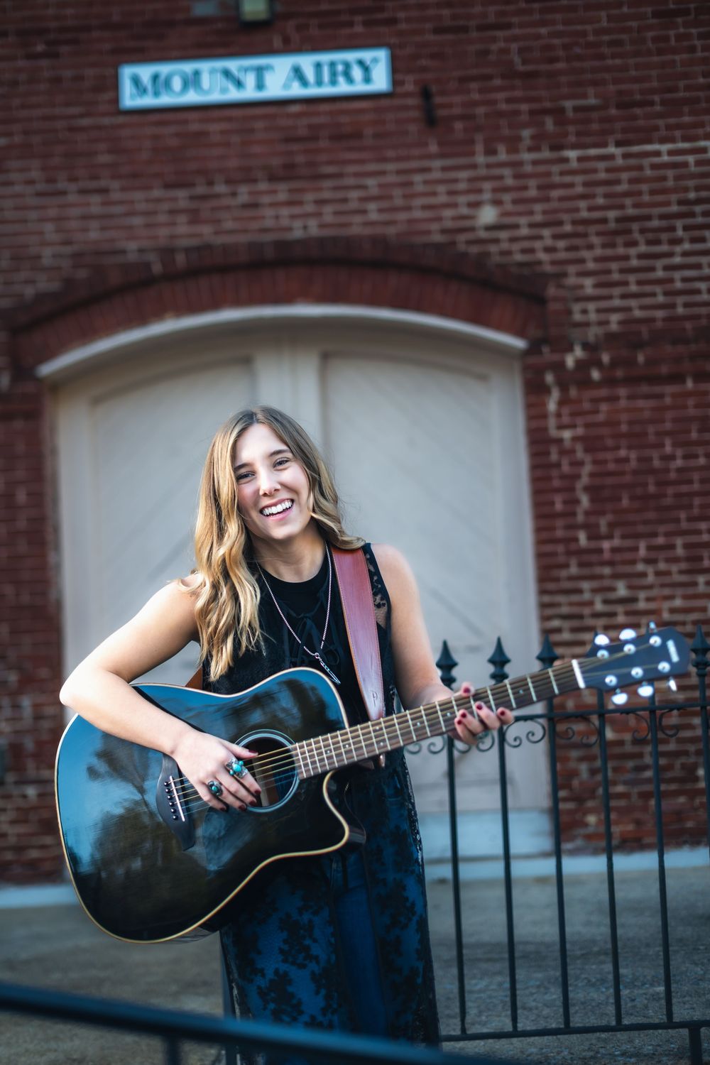Musician in blue dress plays acoustic guitar against brick wall with Mount Airy sign in series of connected photos.