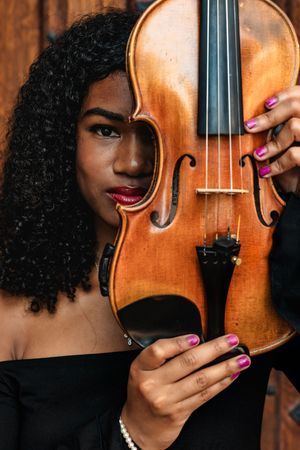 A wooden violin held against a dark background with pink manicured nails visible on the instrument.
