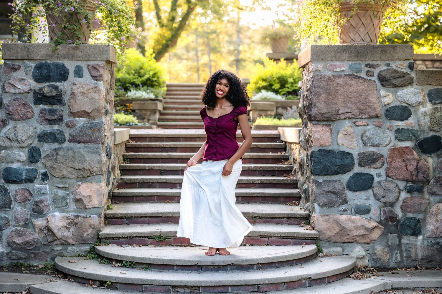 A person in a white dress poses on stone steps in a garden setting during a photo session.