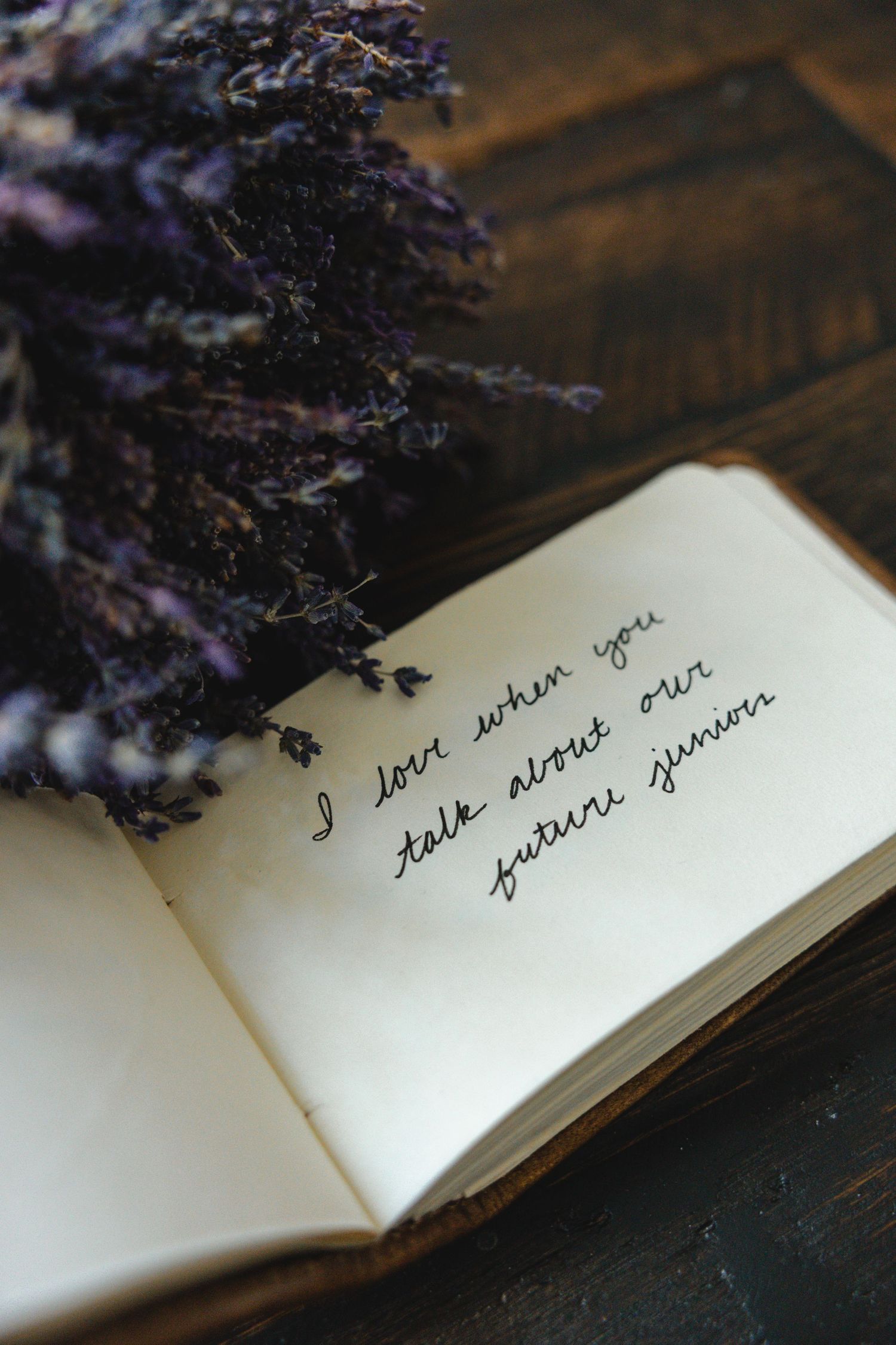Handwritten love note in an open book with dried lavender flowers on a dark wooden surface.
