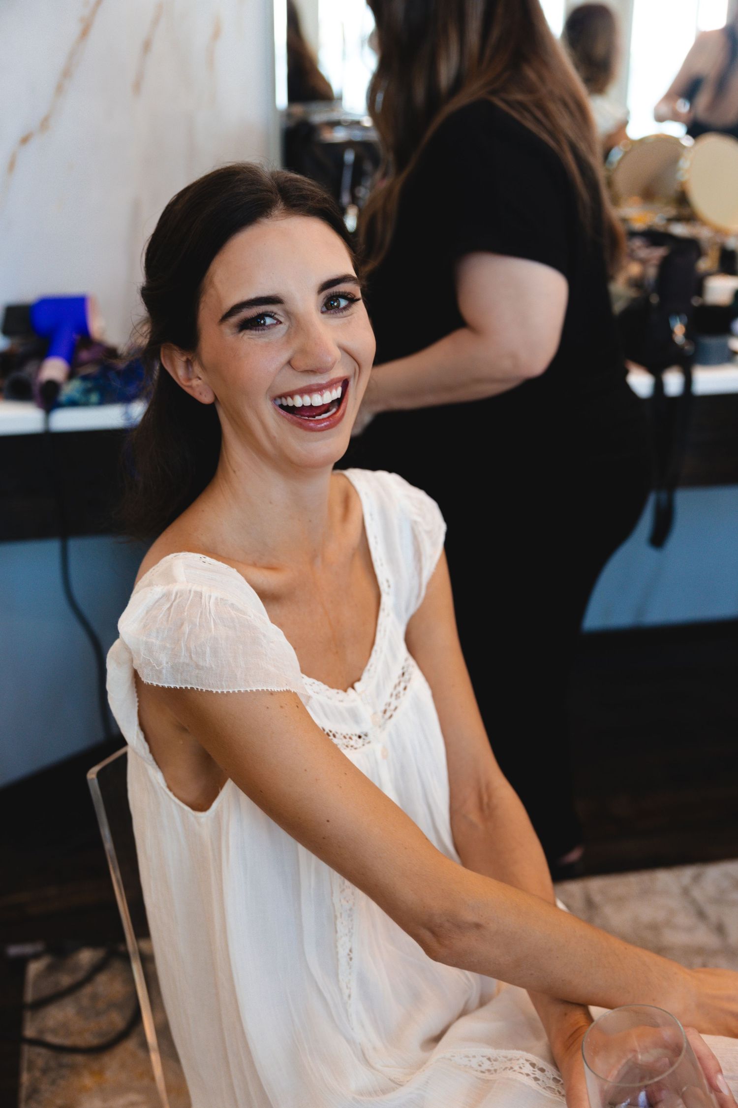 A bride in a white dress laughs joyfully while getting ready for her wedding.