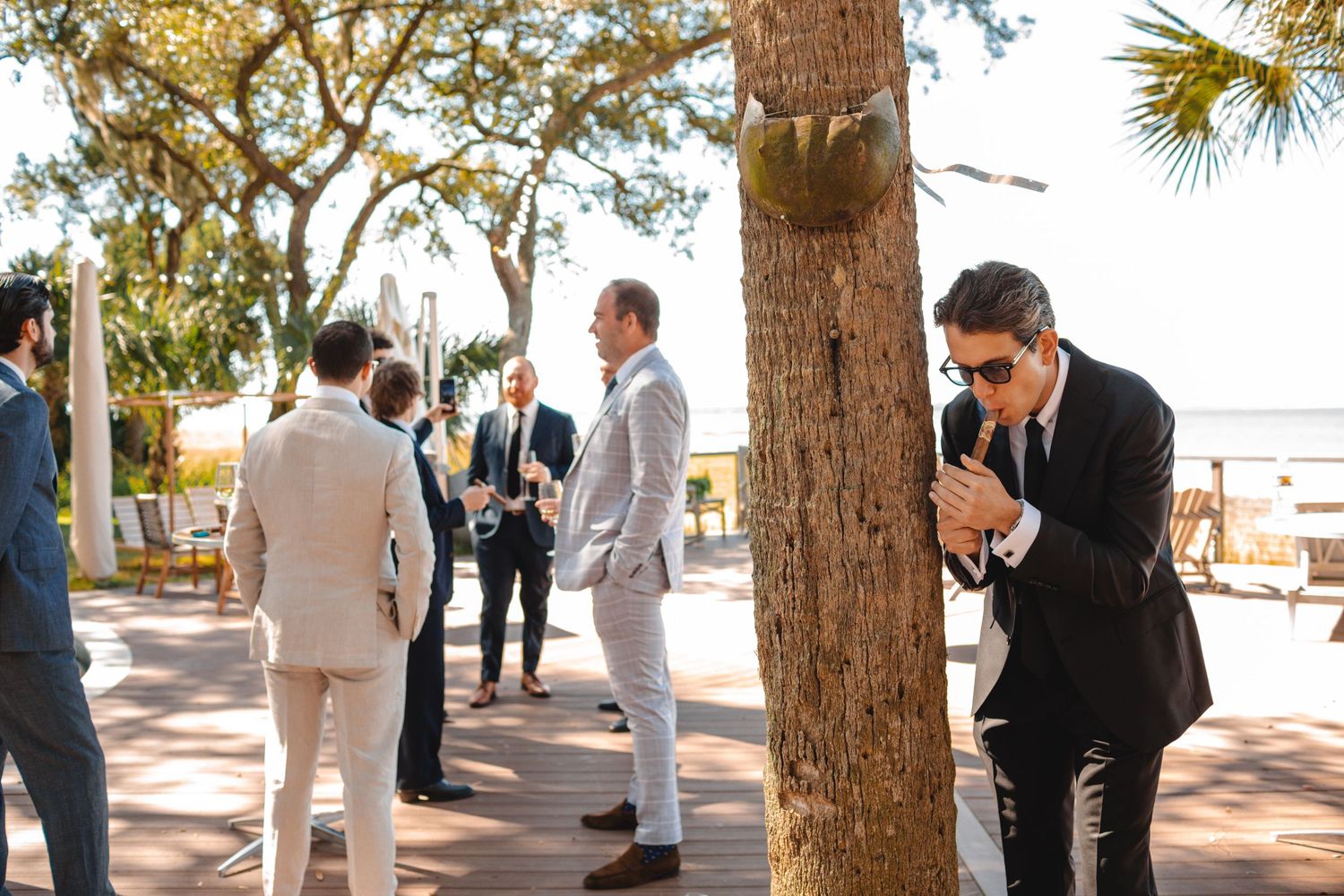 Wedding guests gather under palm trees at an outdoor ceremony venue on a sunny day.