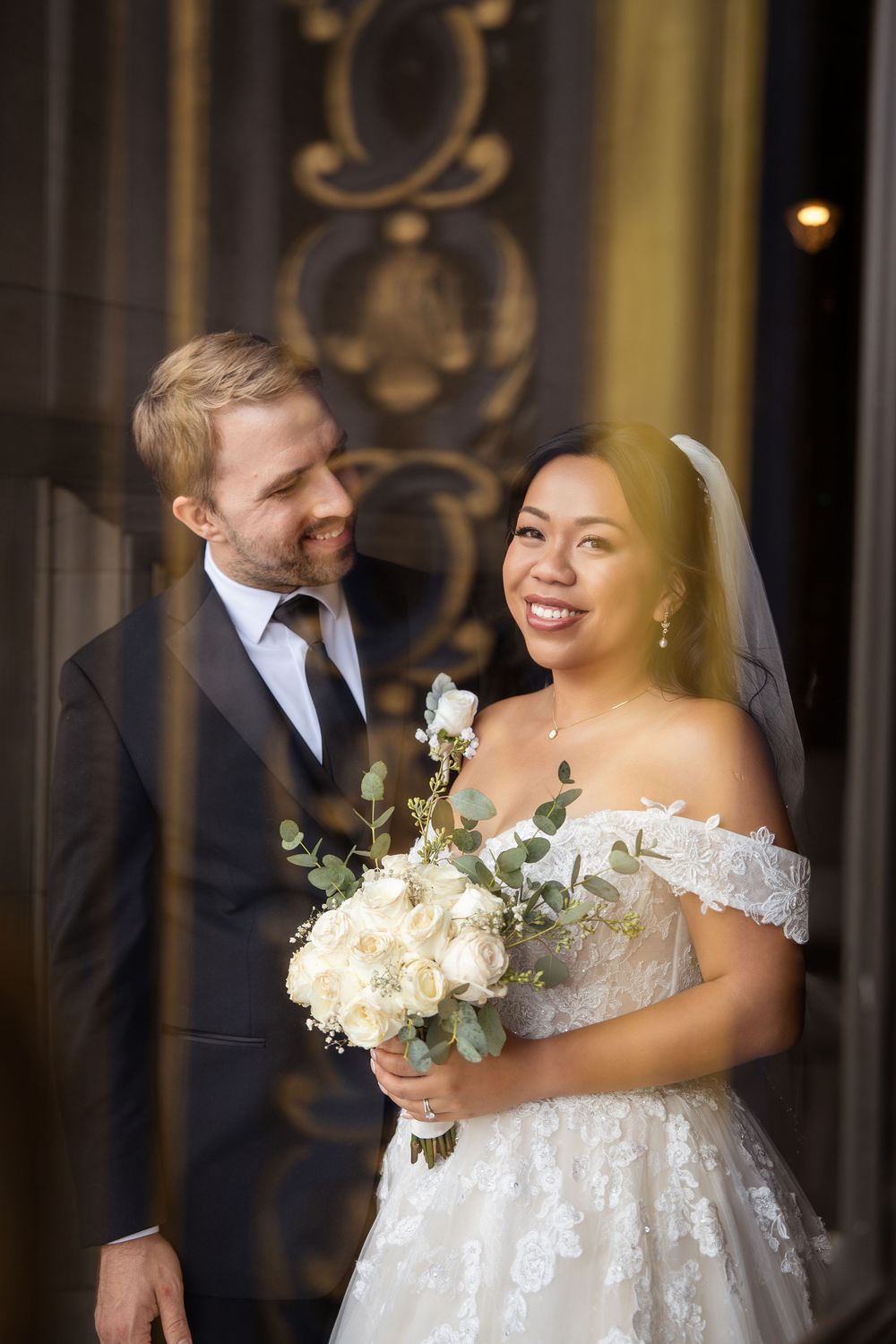 Elegant wedding couple shares joyful moments in a grand hallway with ornate architecture and natural lighting.