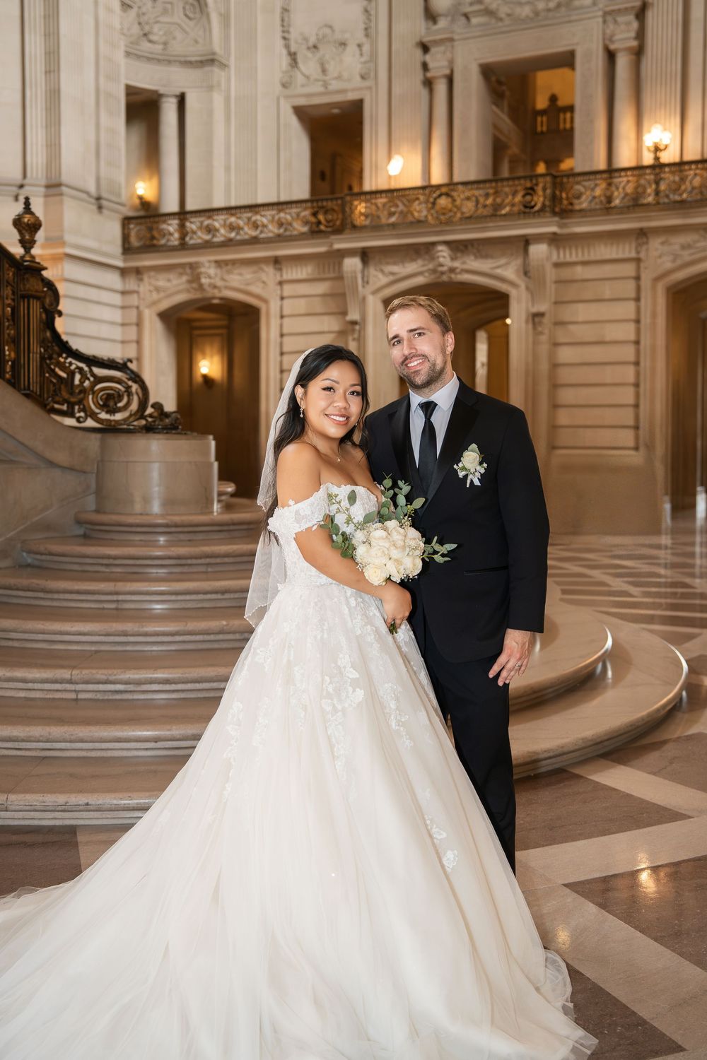 Elegant newlyweds pose on grand marble staircase in historic building with ornate architectural details.