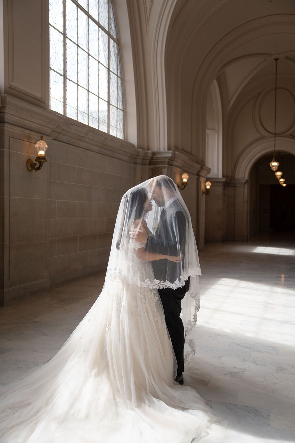 Ethereal bridal portraits with dramatic veil in sunlit corridor with classical architectural details.