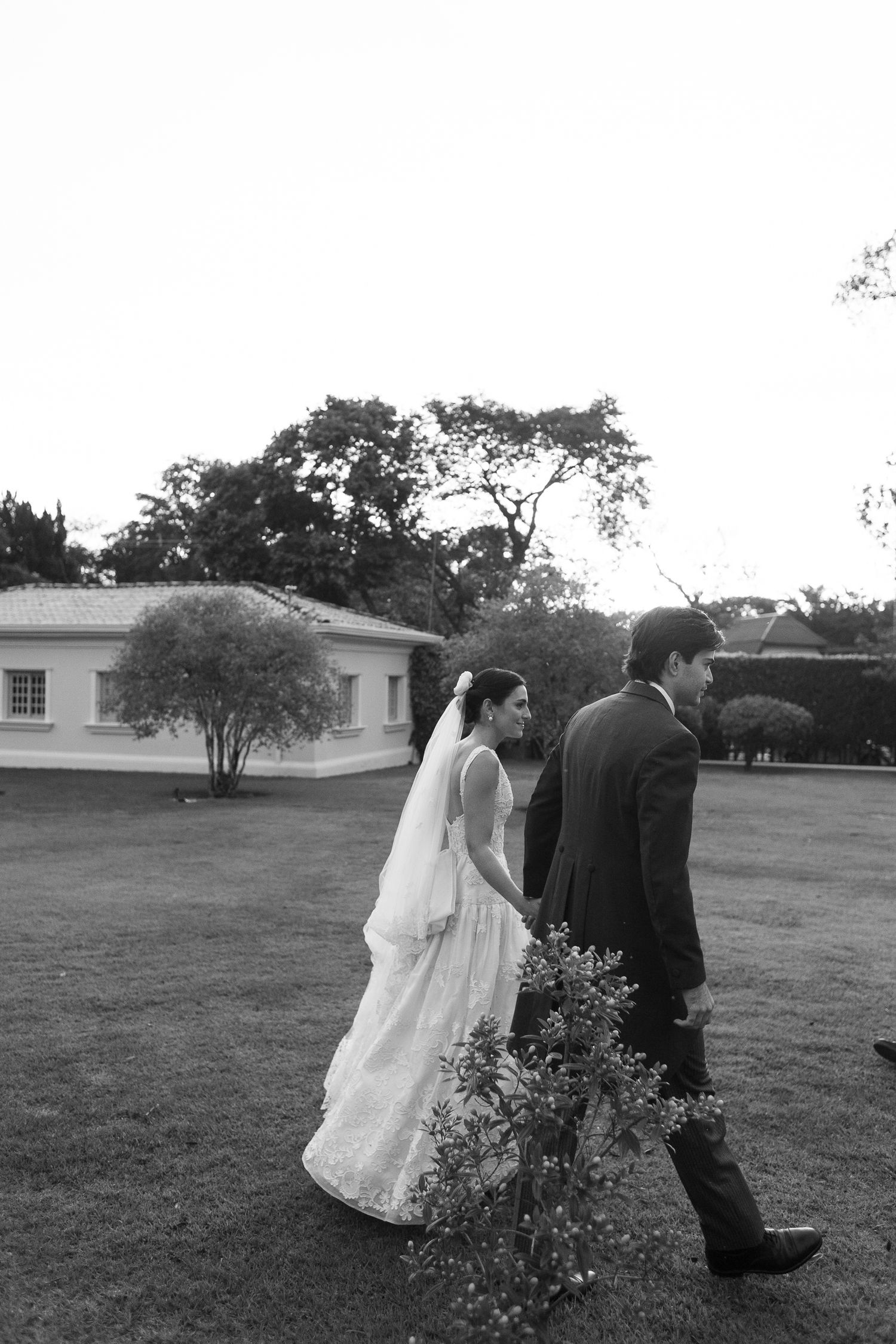 A bride and groom walk together across a grassy lawn during their wedding photo session.