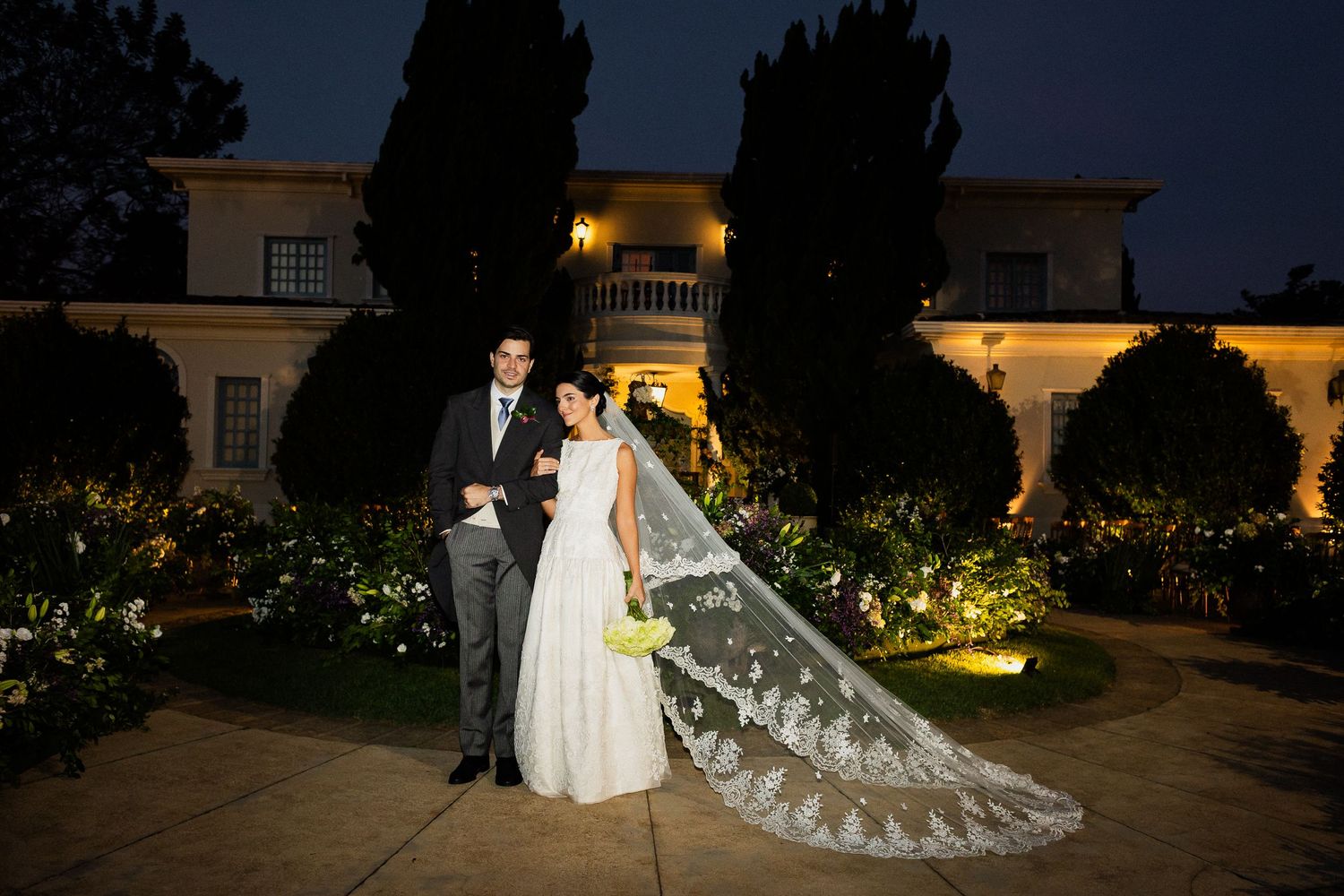 A romantic evening wedding photo sequence showing a couple walking through an illuminated garden at dusk.