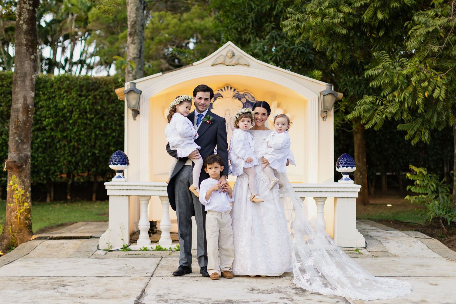 Wedding party poses in front of yellow gazebo in outdoor garden setting during elegant celebration.
