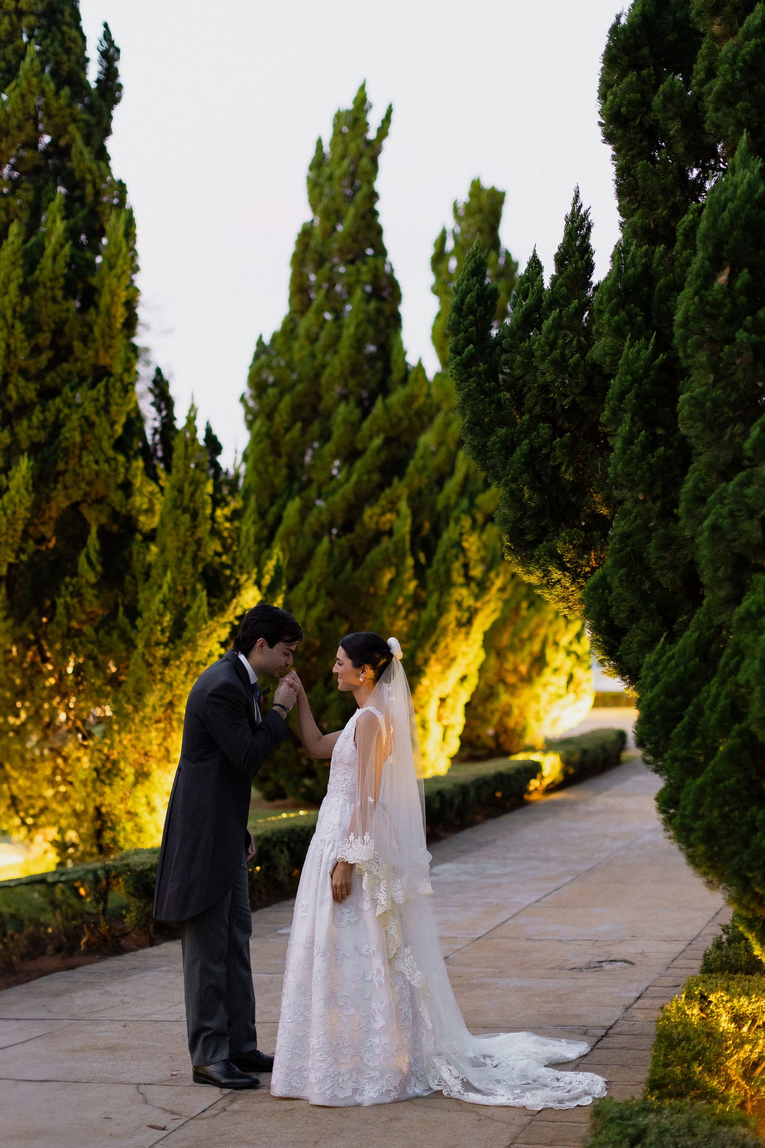 A romantic wedding couple shares intimate moments along a cypress tree-lined path at golden hour.