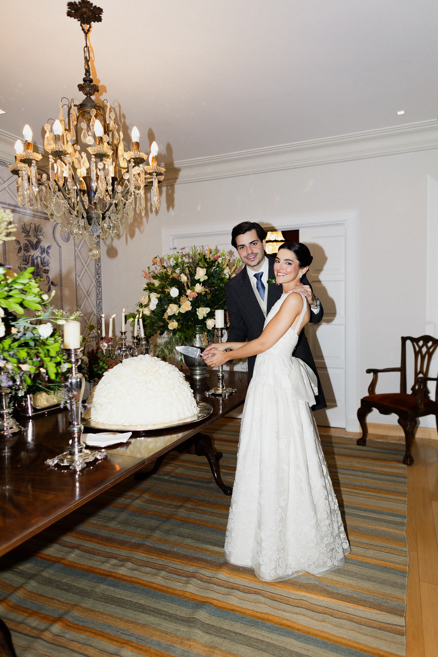 A couple dances together in an elegant room with chandeliers and floral arrangements on display.