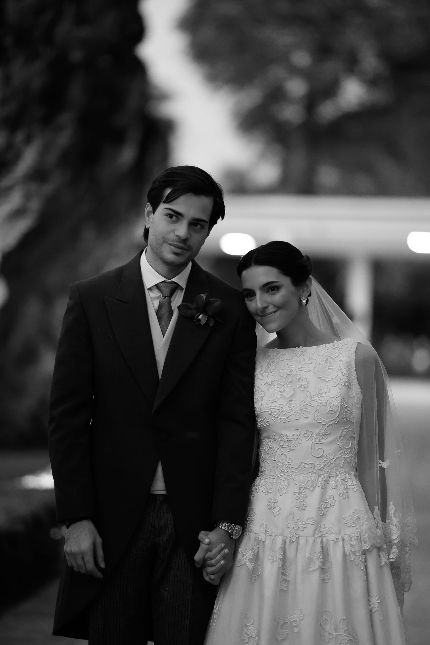 A black and white wedding photograph showing a couple holding hands outdoors at dusk.