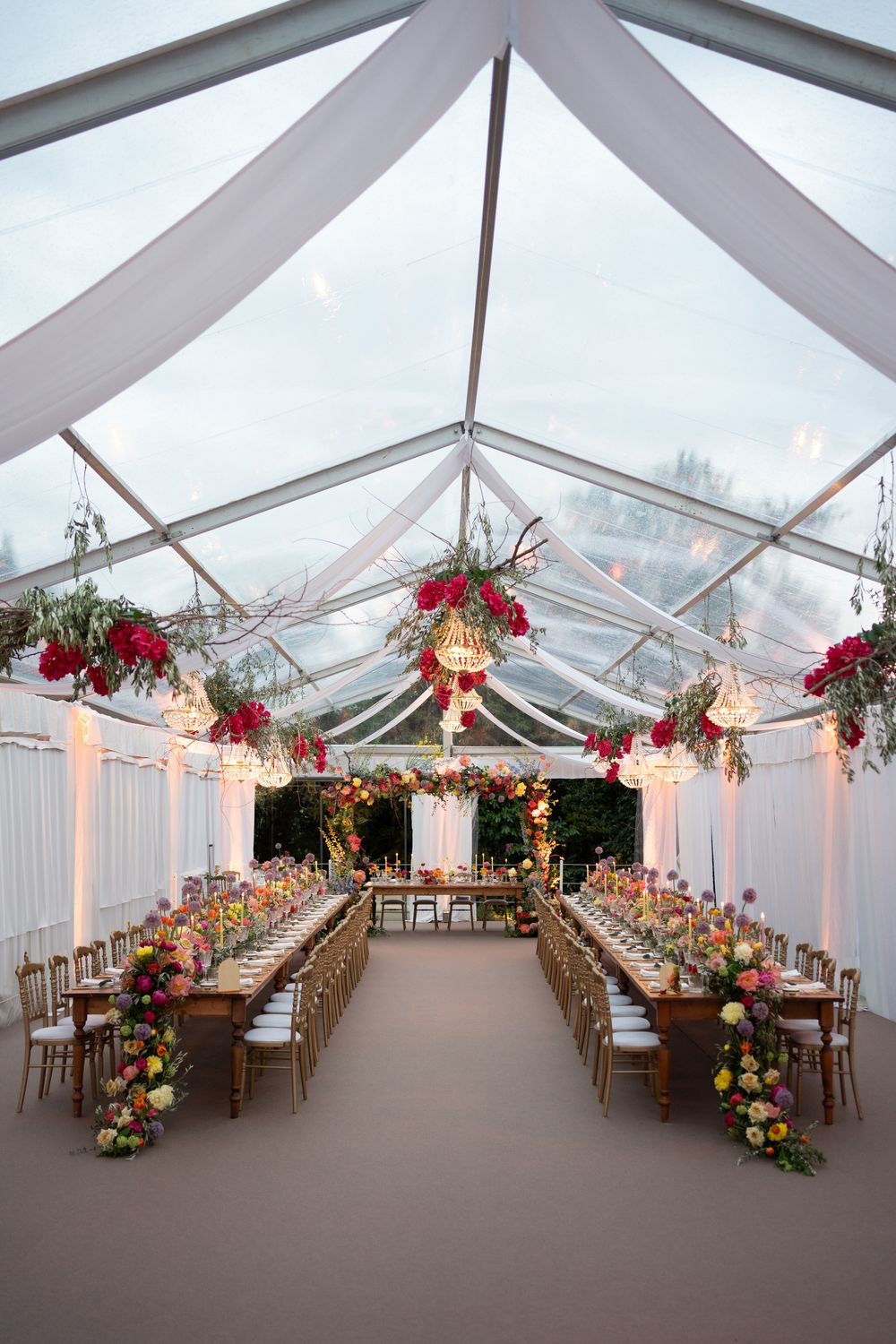 Clear tent wedding reception setup with elegant floral arrangements and string lights creating a romantic atmosphere.