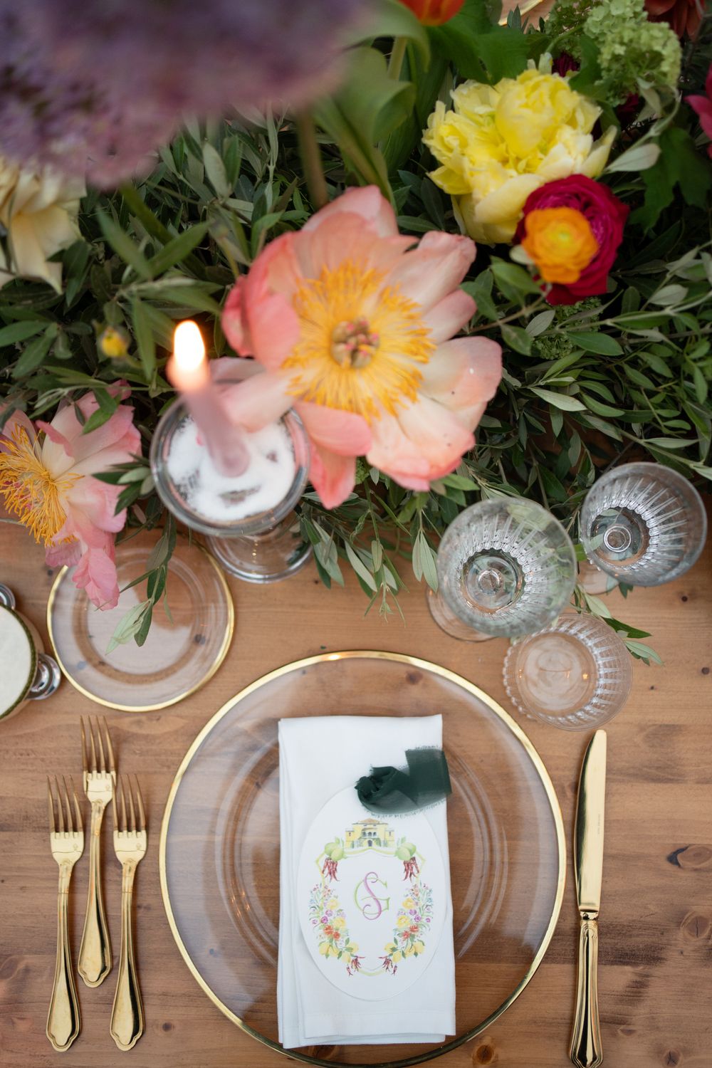 Elegant table settings with gold cutlery, crystal glasses, and floral arrangements featuring pink and yellow blooms on wooden table.