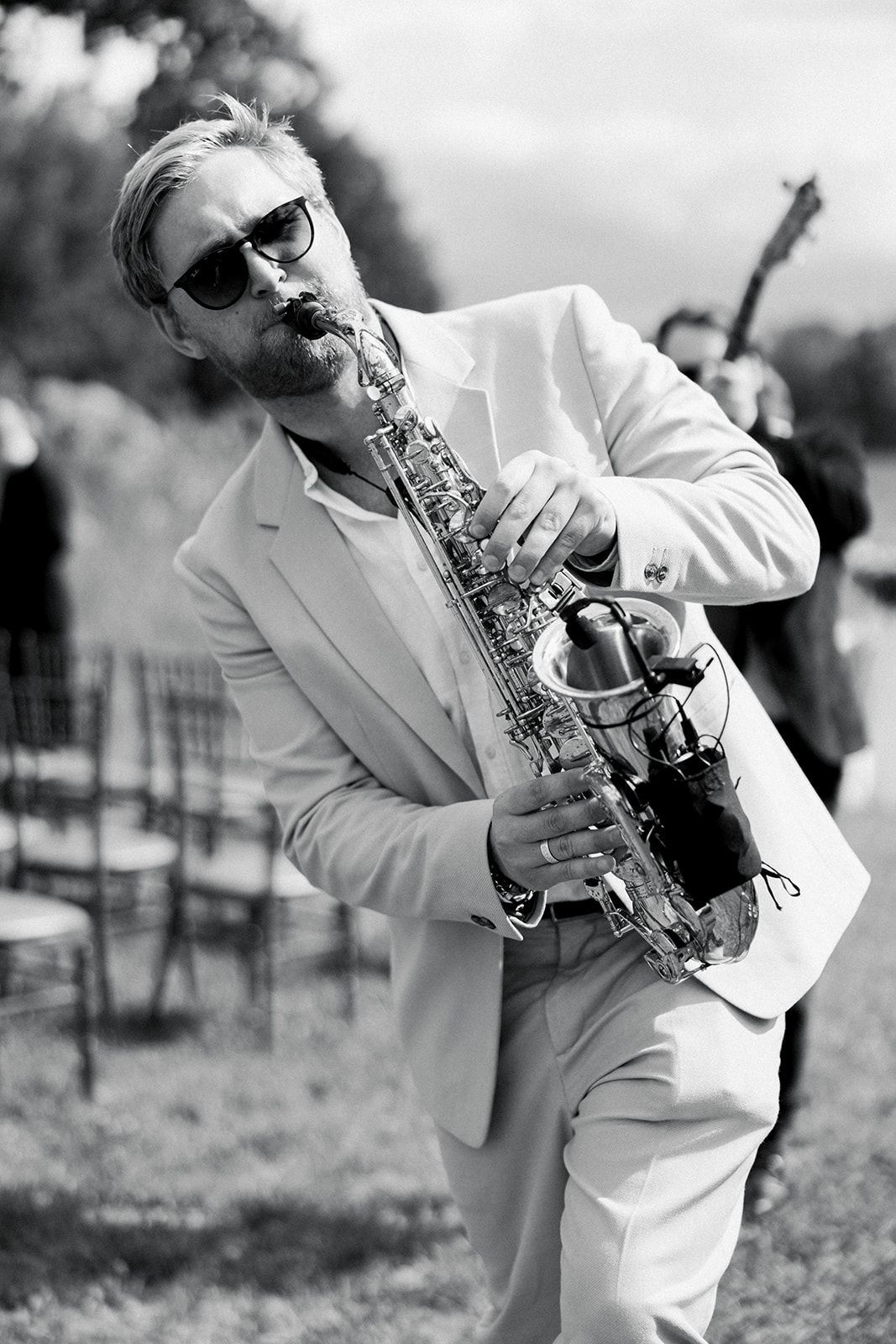 A musician in a white suit plays saxophone outdoors in a series of dynamic black and white performance shots.