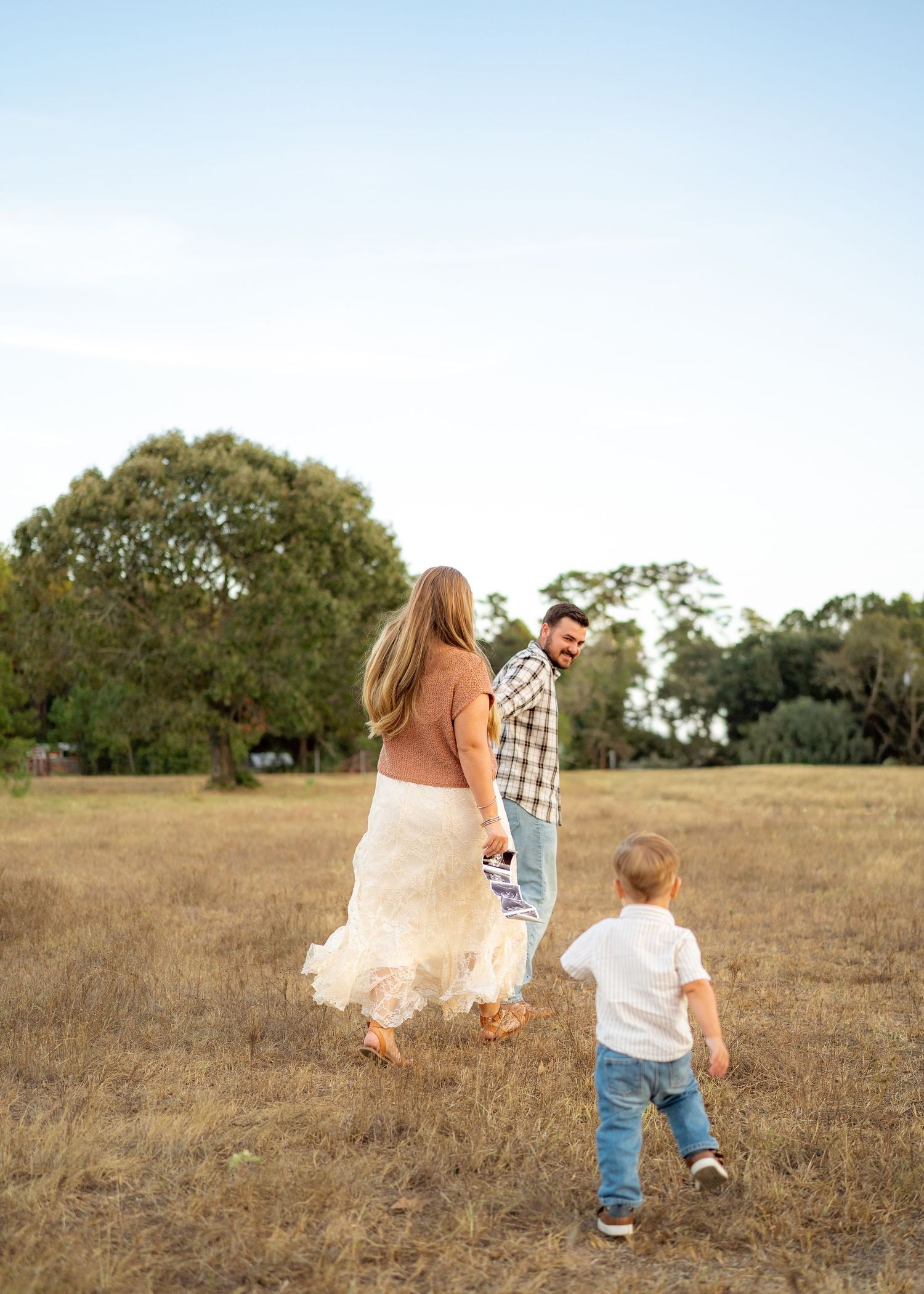 Candid moment of the Emersons walking hand-in-hand with their toddler during a maternity announcement session.