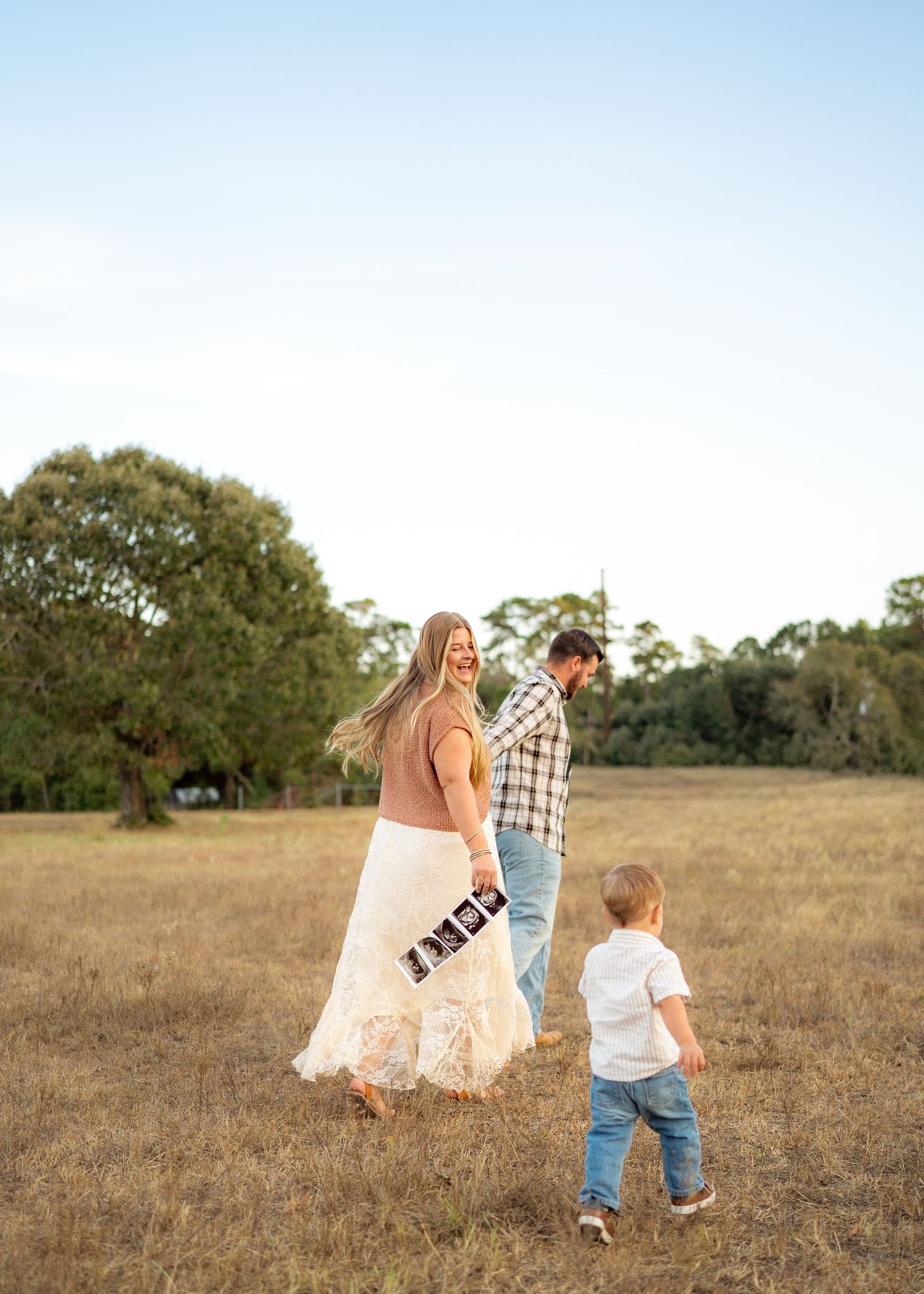 Candid moment of the Emersons walking hand-in-hand with their toddler during a maternity announcement session.