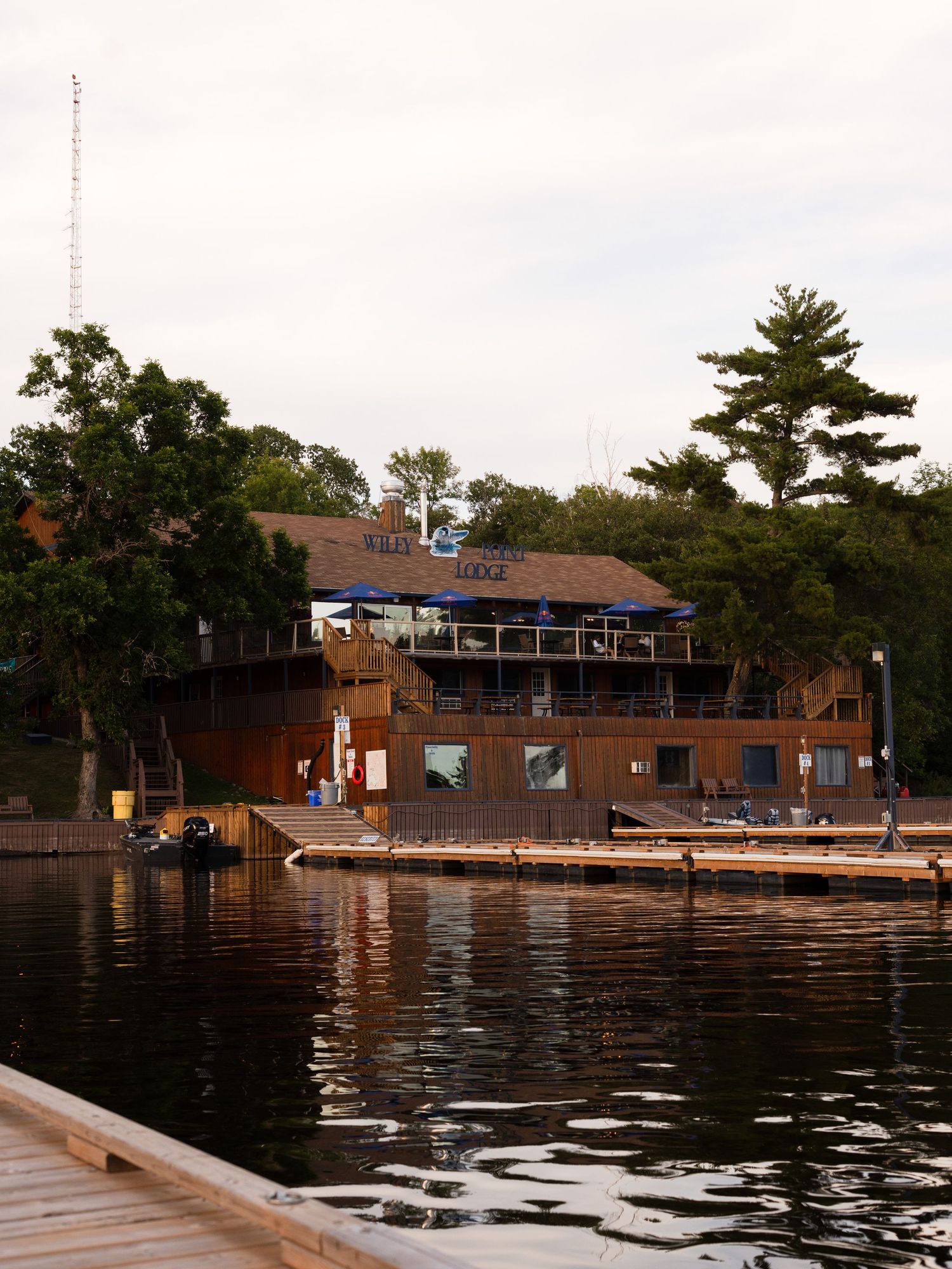 Rustic lakeside restaurant with wooden deck and docks reflecting on calm water.