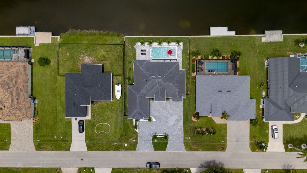 Aerial view of waterfront homes with pools and lush green lawns along a canal in a Florida neighborhood.