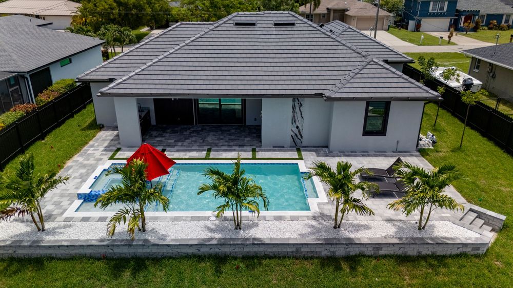 Aerial view of a modern gray home with a pool, palm trees, and a red umbrella in Florida.