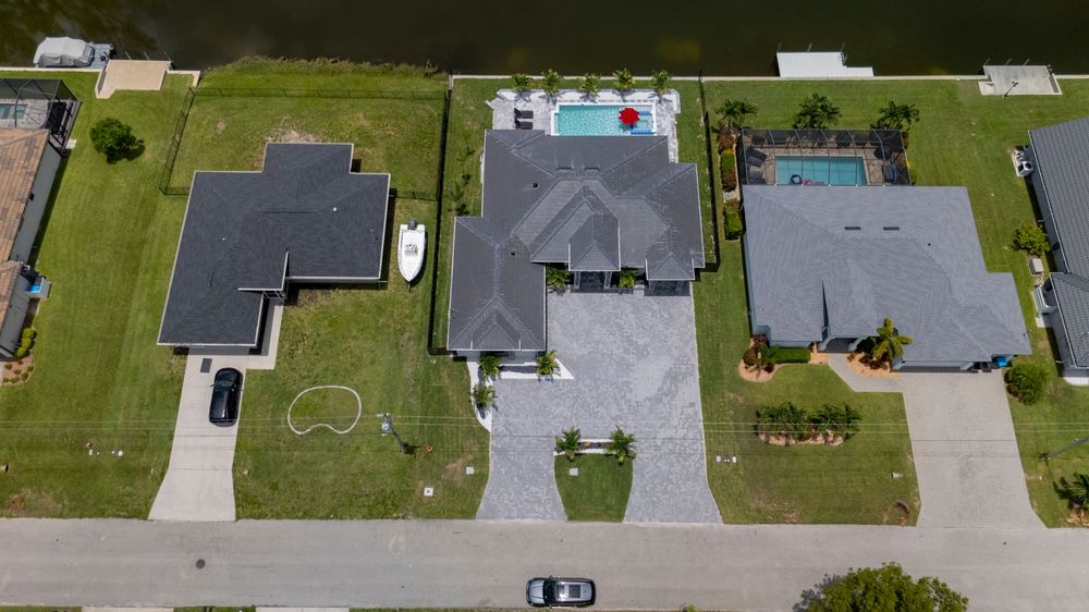 Aerial view of three waterfront homes with pools and green lawns along a Florida canal.
