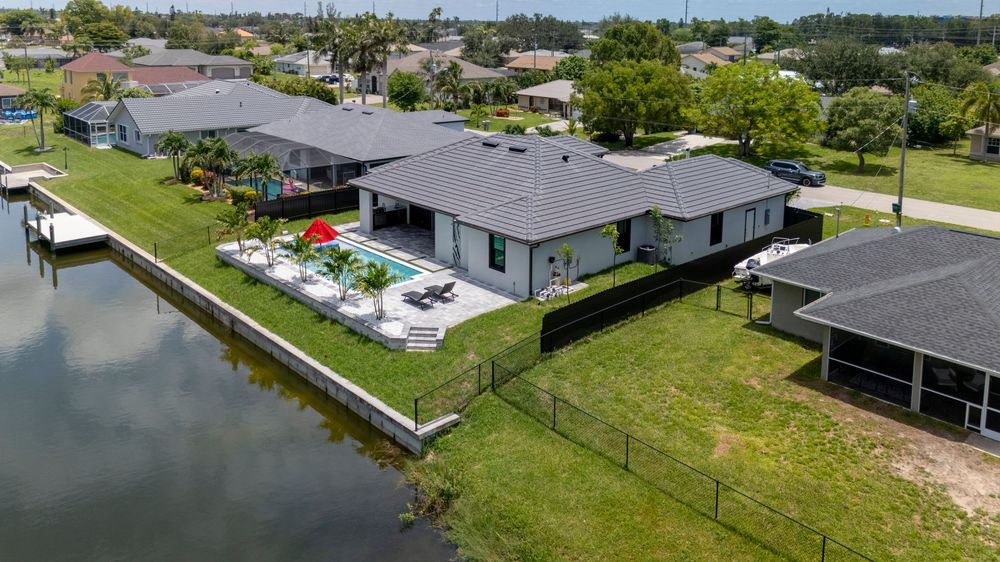 Aerial view of a modern waterfront home with a pool, patio furniture, and canal access in Florida.