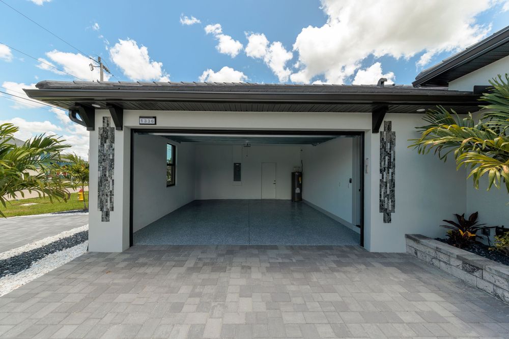 Open two-car garage with decorative columns, epoxy floors, and a paver driveway on a modern home.