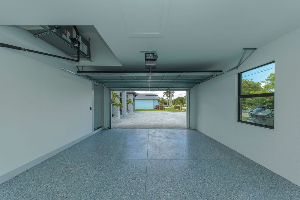 Spacious two-car garage interior with epoxy flooring, garage opener, and a window view outside.