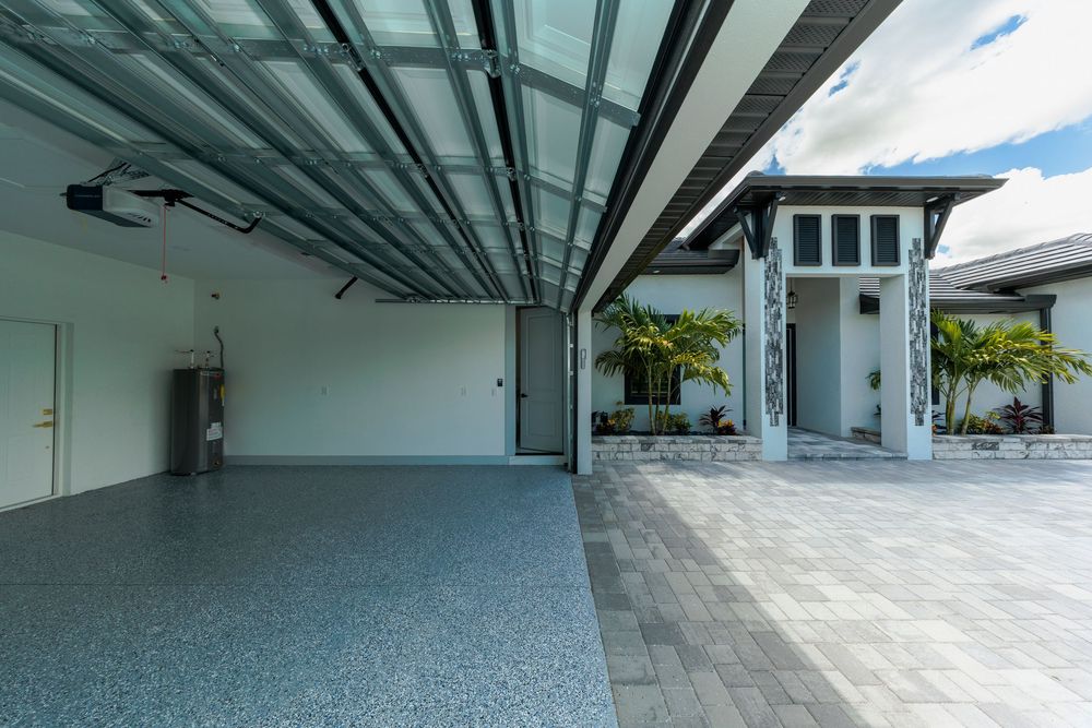 Modern home garage interior with epoxy floors, glass panel door, and view of paver courtyard.