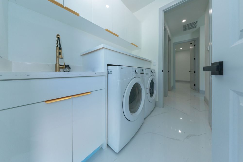 Bright white laundry room with front-load washer and dryer, built-in cabinetry, and gold hardware accents.